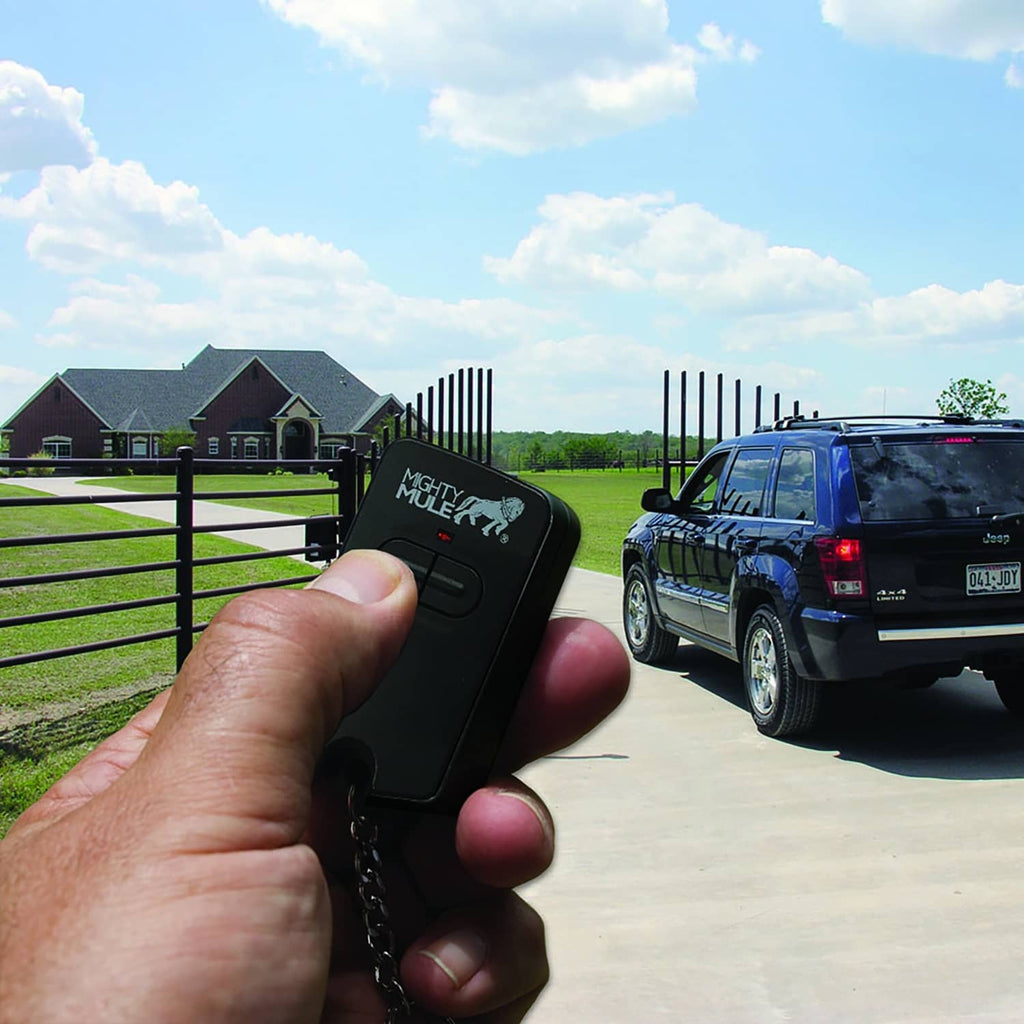 Hand holding a black Mighty Mule gate opener remote near a parked vehicle
