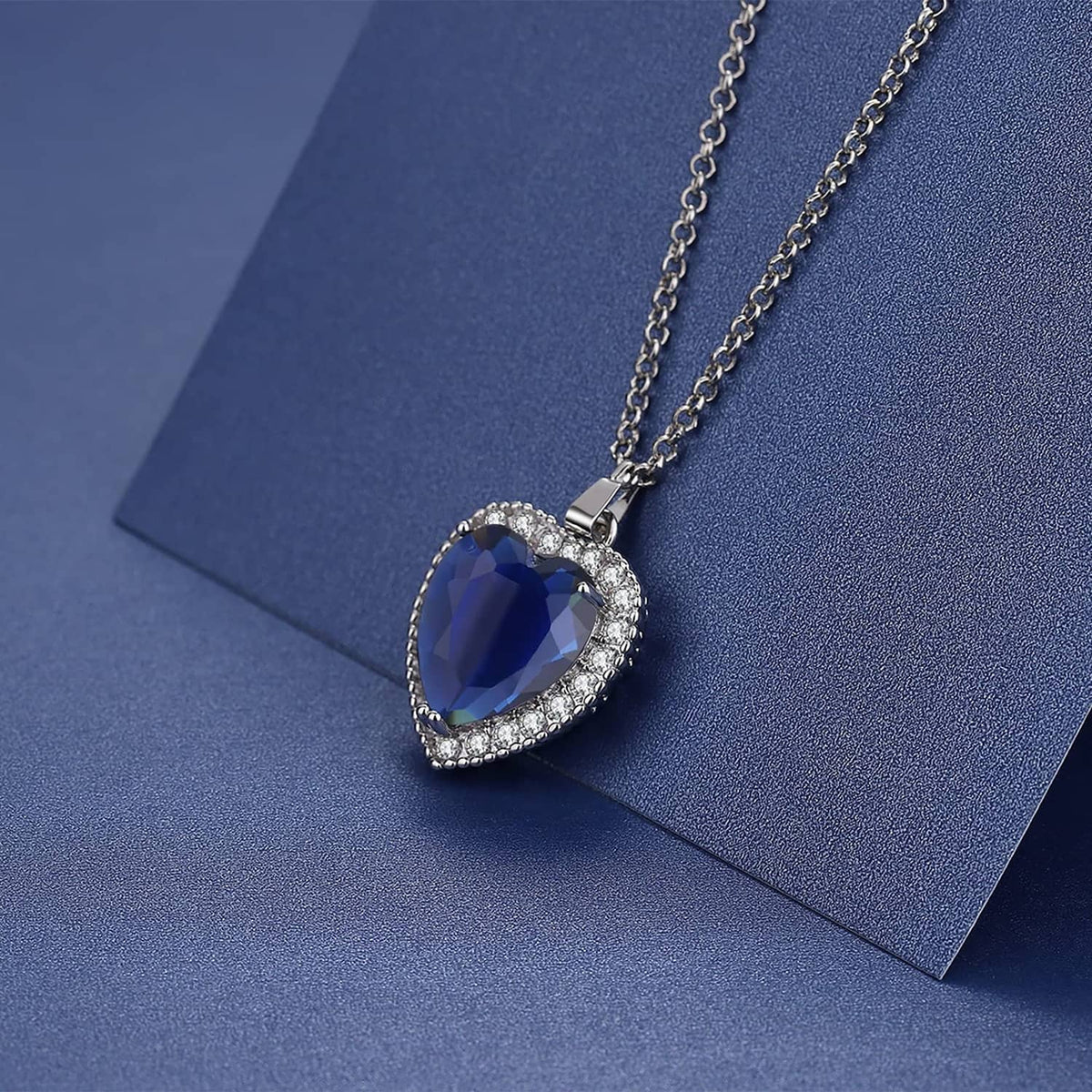 Blue heart pendant necklace on chain, shown resting on a blue surface