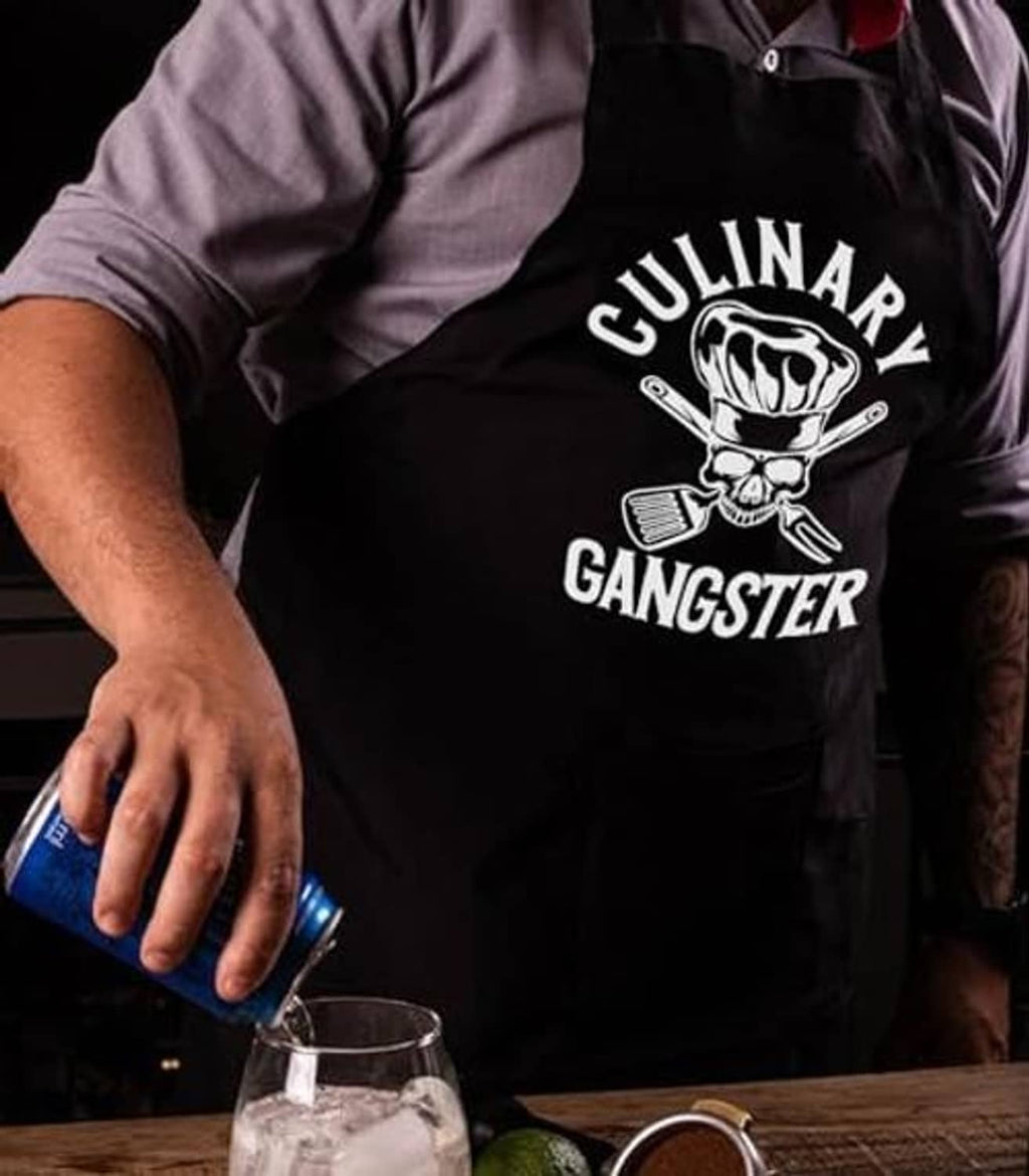 Black cooking apron with skull and utensils graphic, worn by chef with hands.