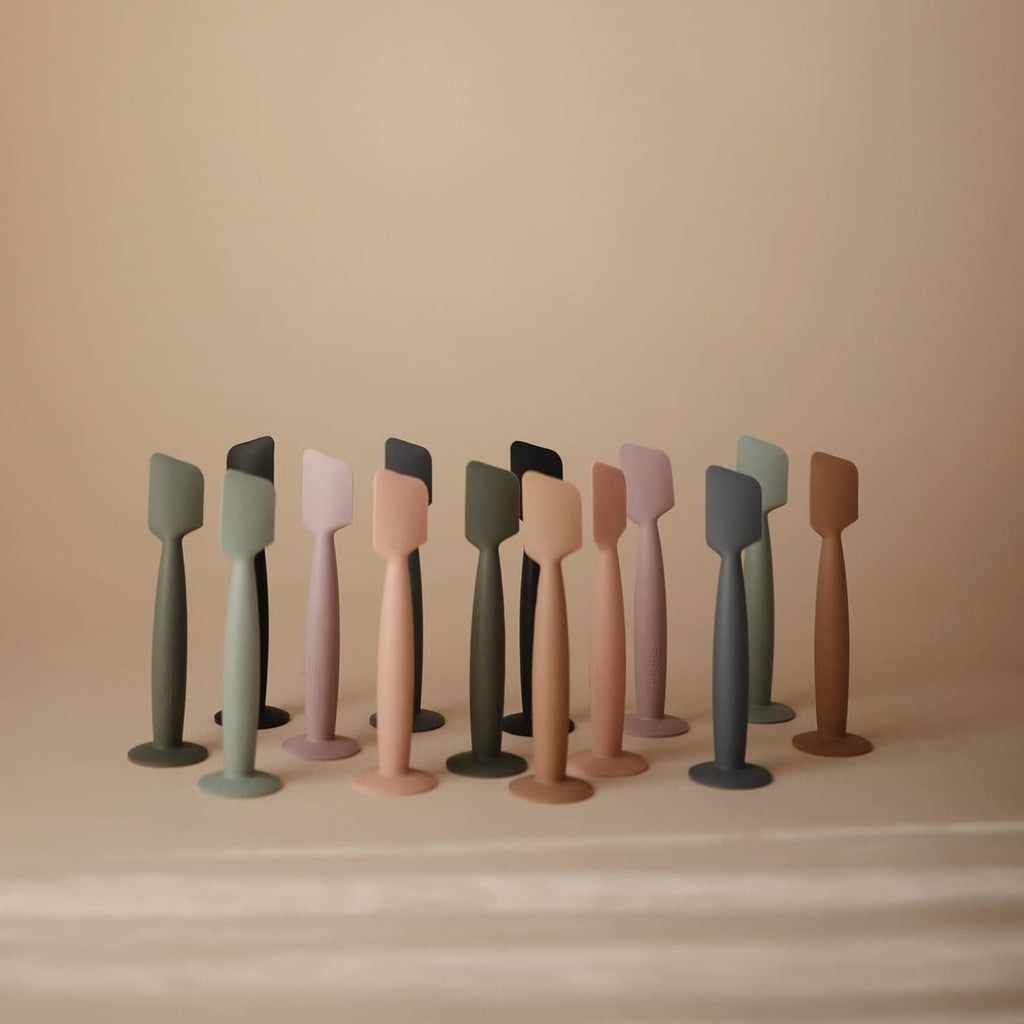 Row of Mushie soft silicone diaper cream applicators in multiple colors
