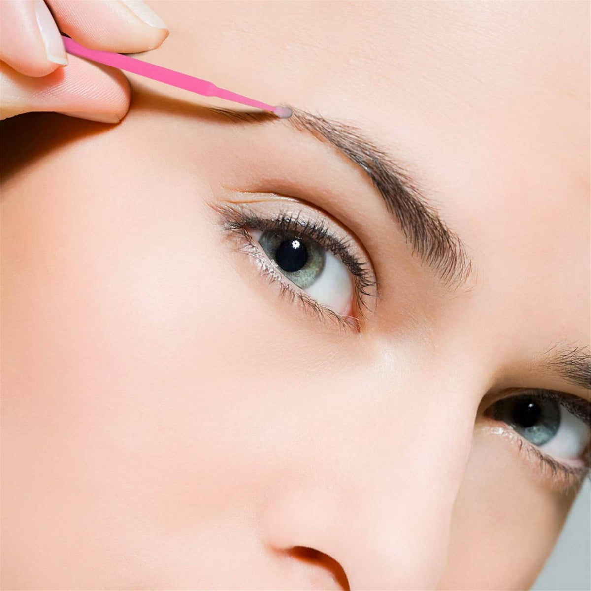 Pink micro cotton swab held by hand near the eye for eyelash or brow touch-ups