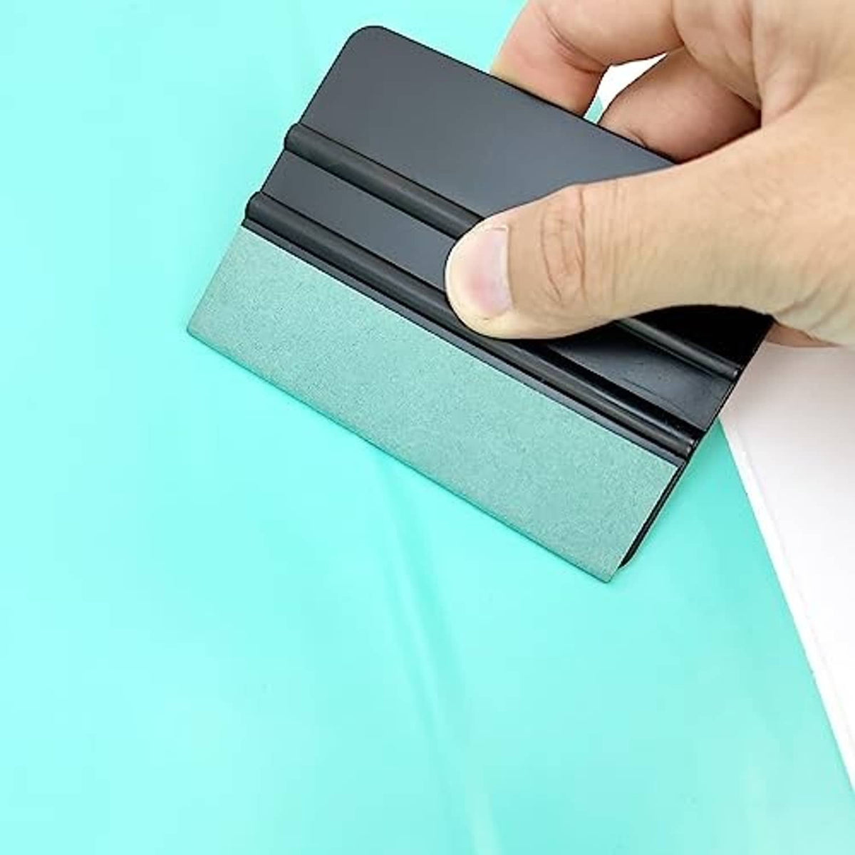 Hand using window film squeegee with teal felt pad and black handle base