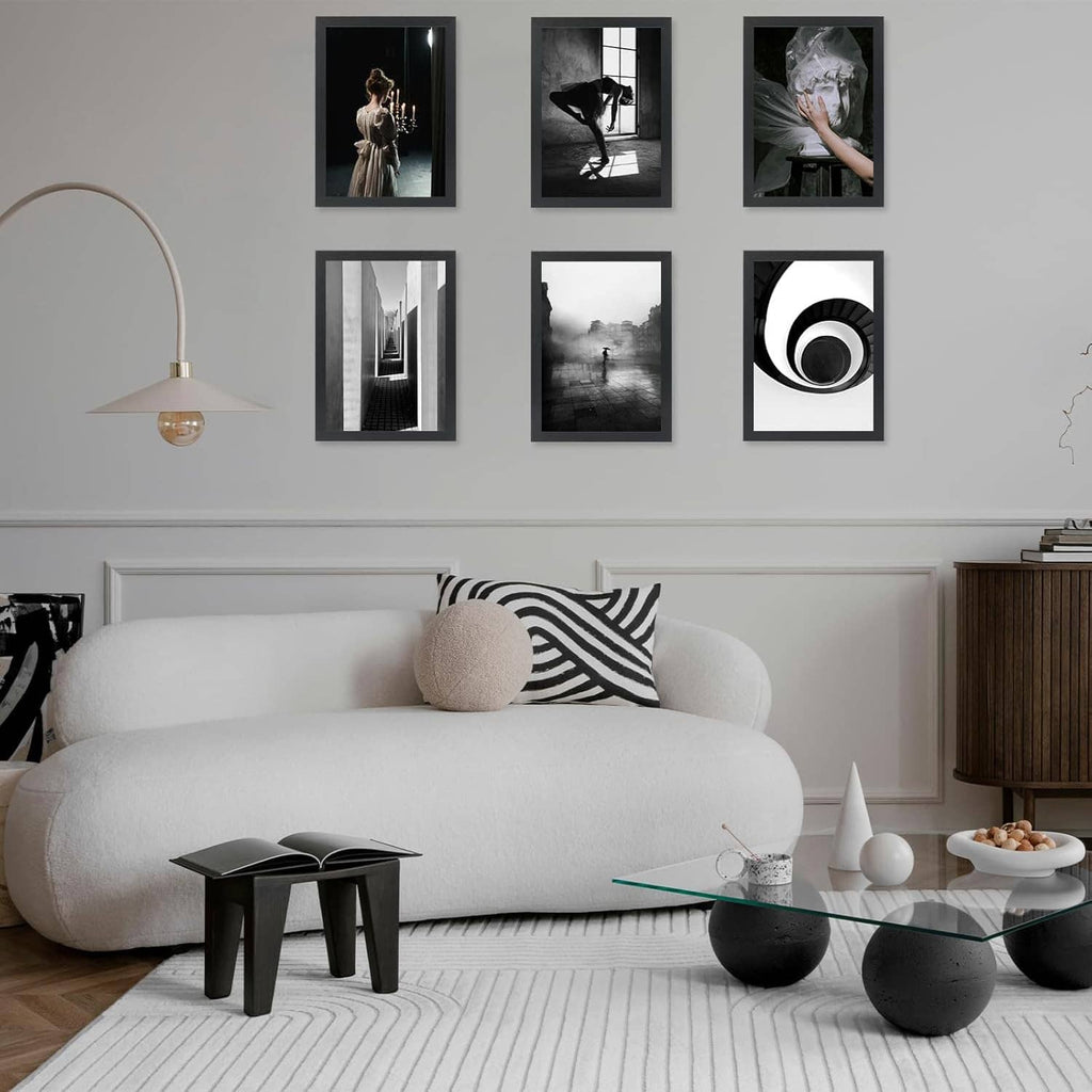 Set of black 10x15 picture frames on a wall above a sofa with multiple photos.