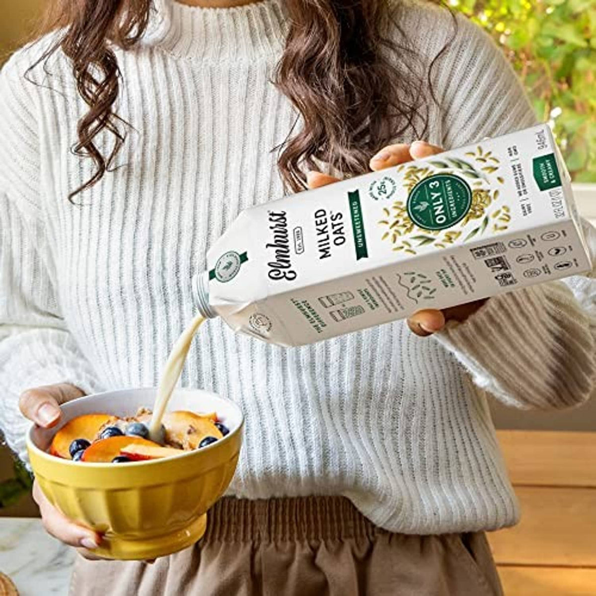Unsweetened oat milk carton held by person with bowl of oats.