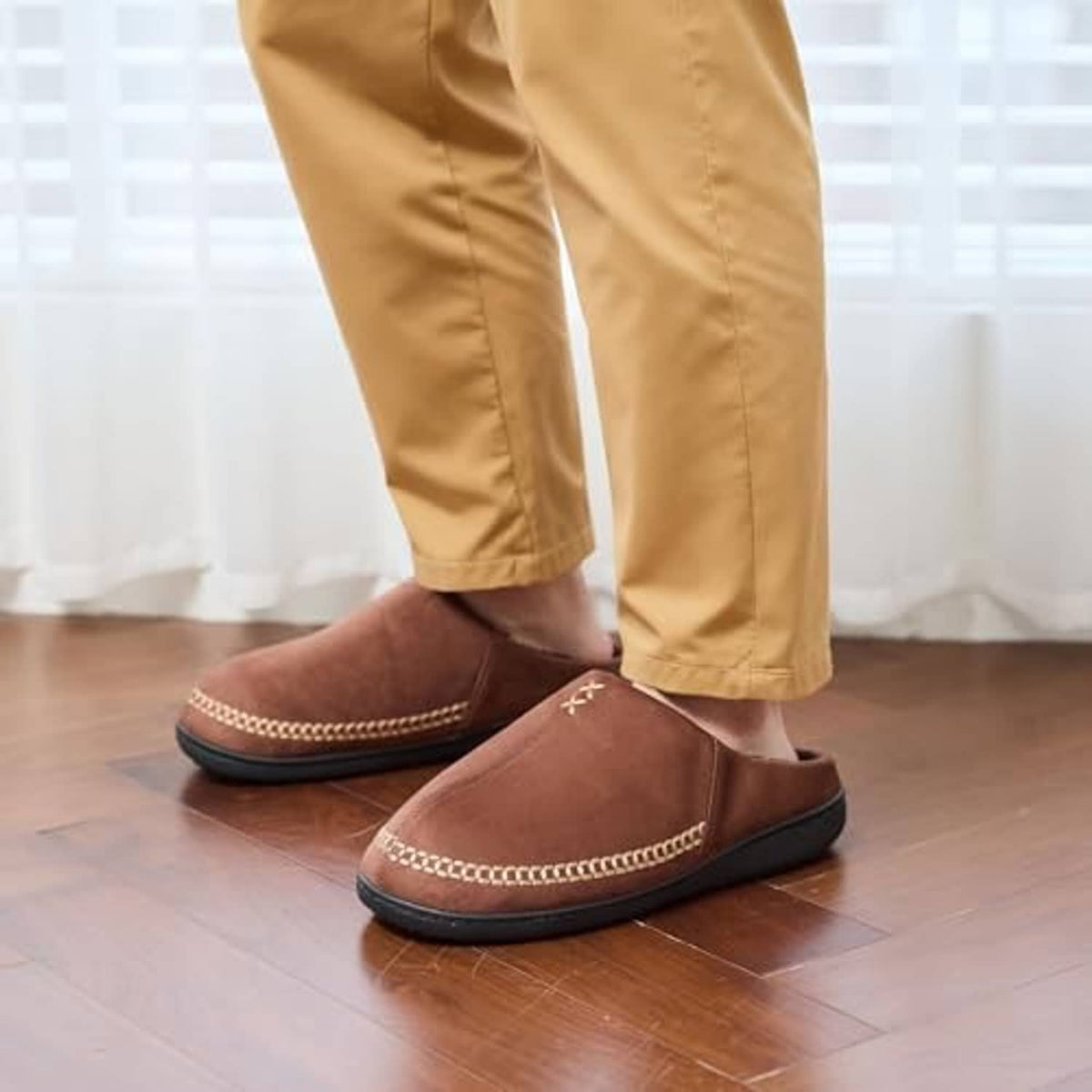 Coffee-brown slip-on moccasin slippers on the floor with black cushioned interior lining