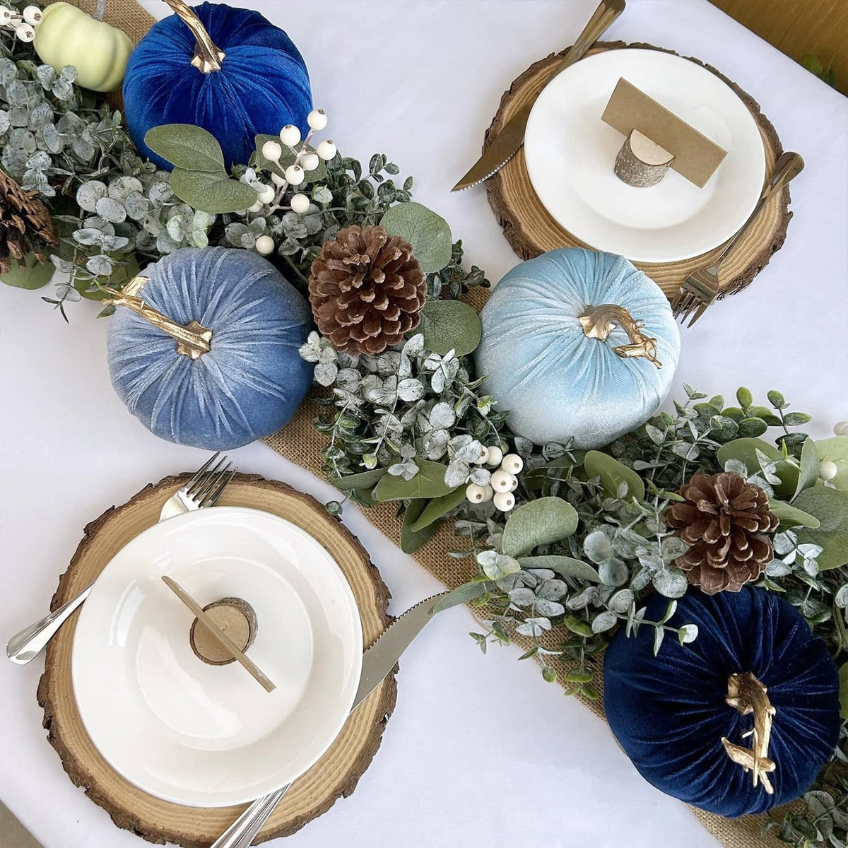 Assorted blue faux velvet pumpkins with gold stems and hanging loops, styled with pinecones