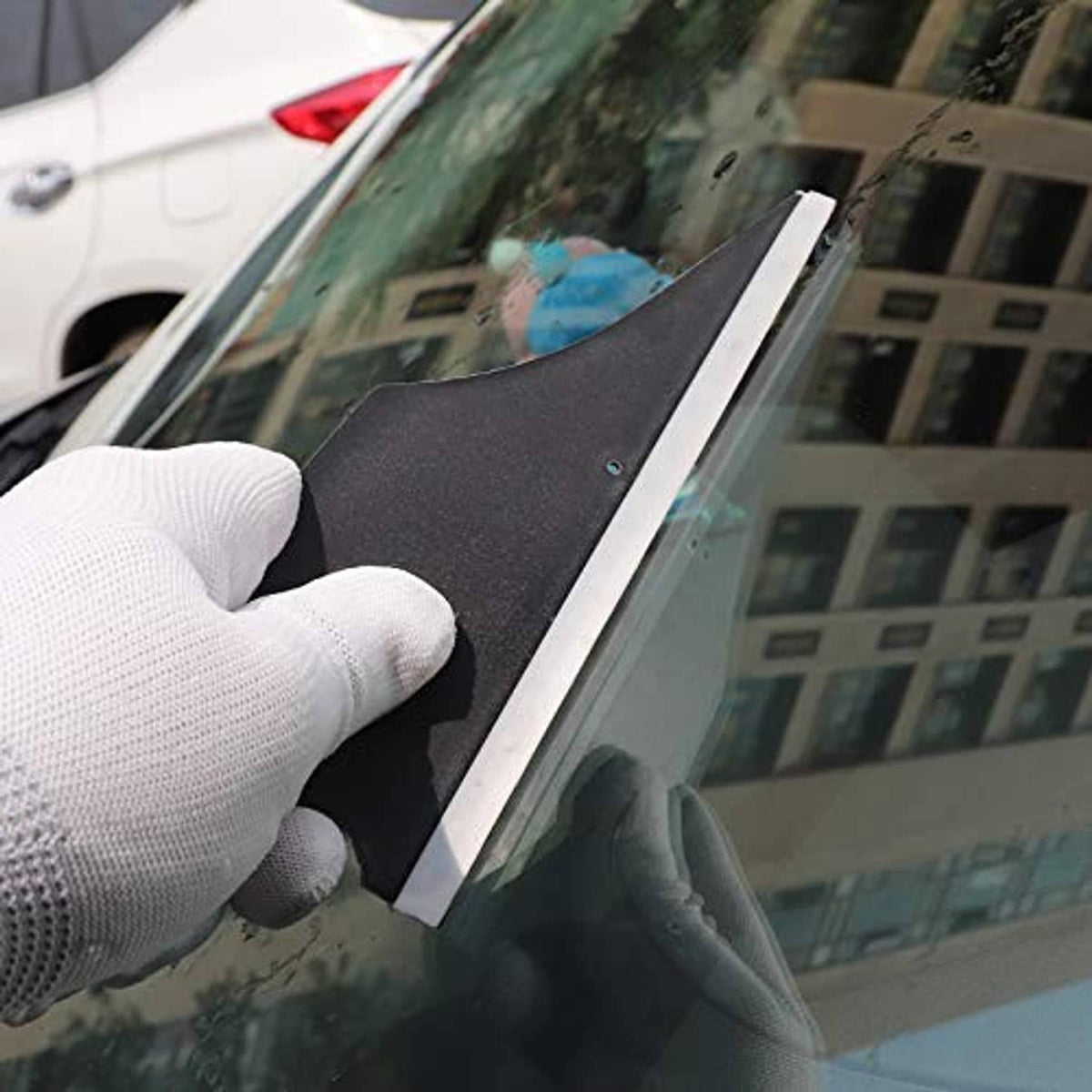 Gloved hand pressing corner squeegee on car windshield glass