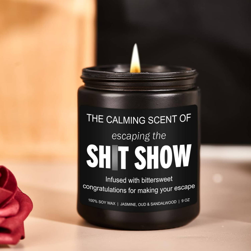 Black jar candle with lit wick and bold white label, held in hand; soy wax, 9 oz.