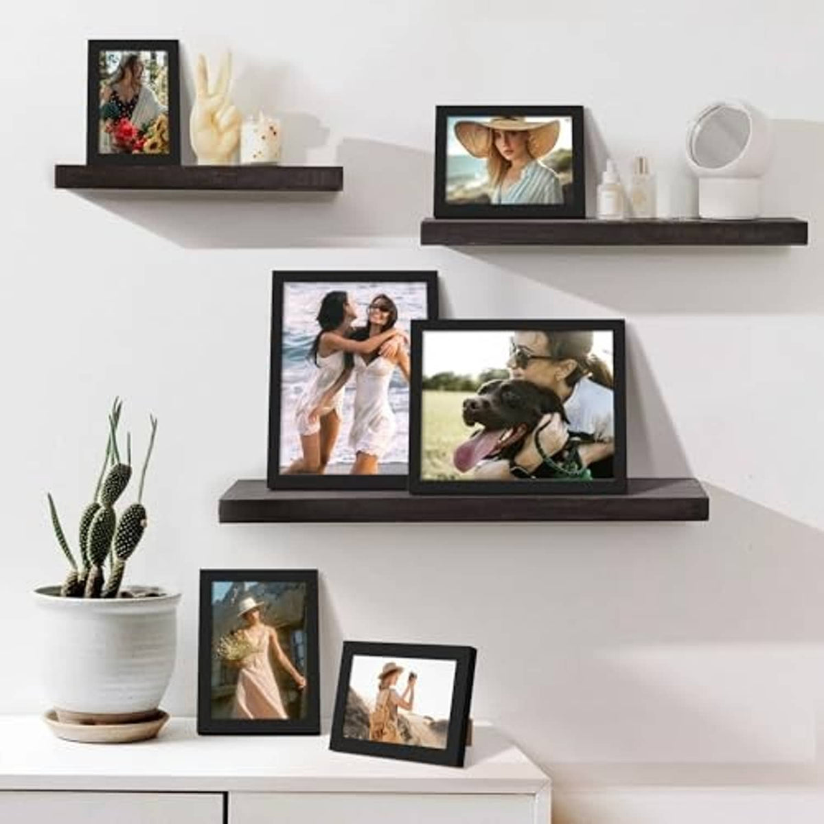 Black picture frames displayed on wall shelves with photos and small decor