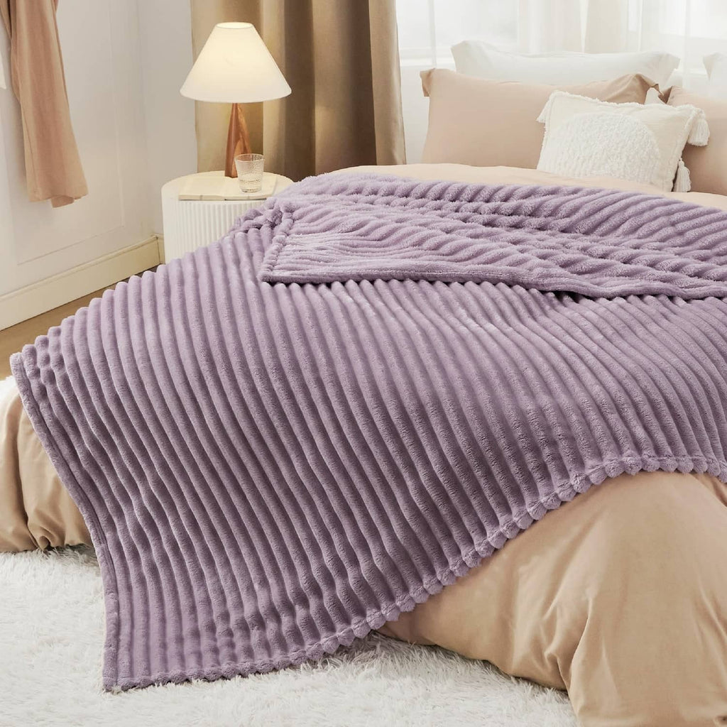 Light purple ribbed fleece blanket folded over a bed, smooth plush top edge