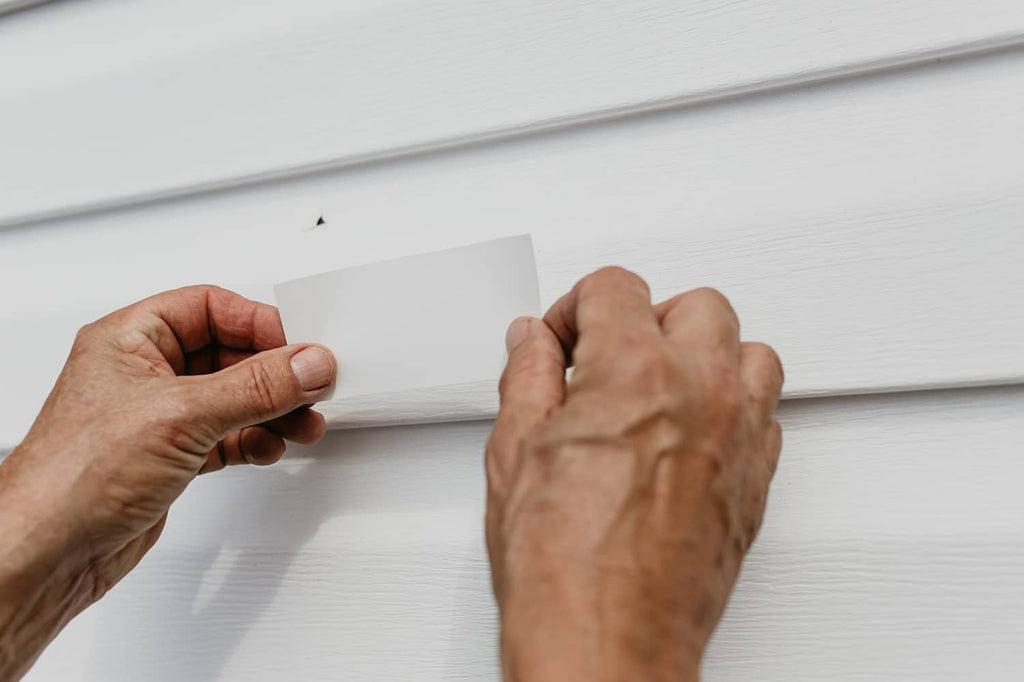 Mendyl vinyl siding repair: hands applying a patch to white vinyl siding