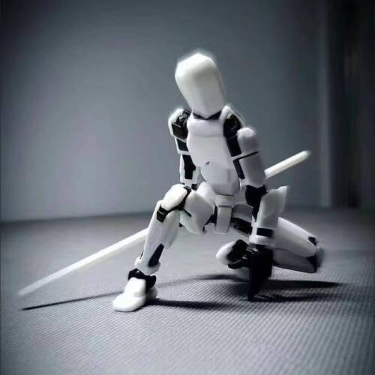 White articulated robot action figure kneeling with a long black and silver weapon