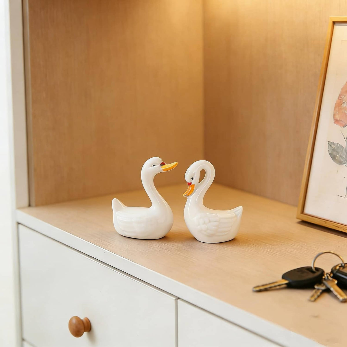 Two white ceramic swan figurines standing on a shelf