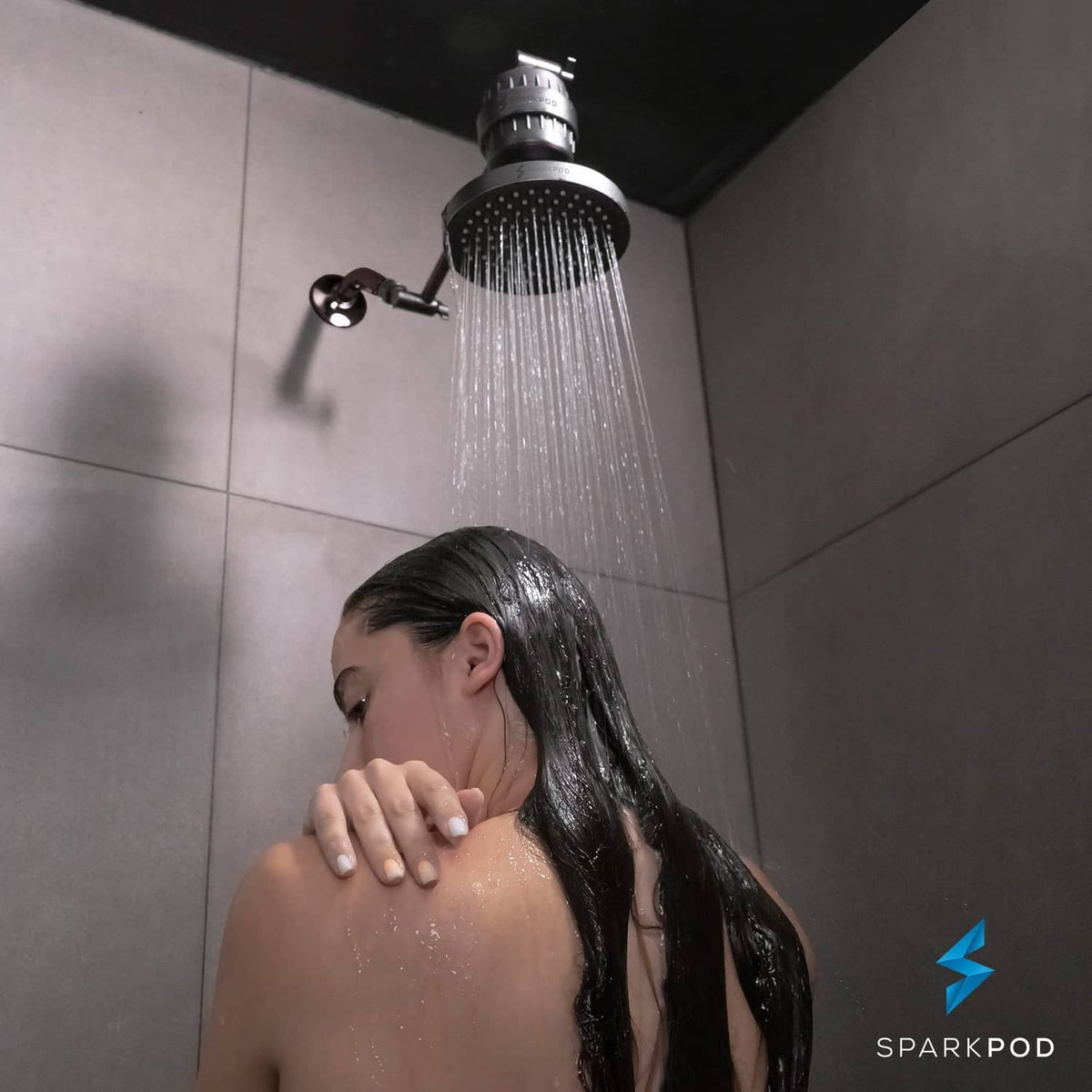Person under oil rubbed bronze rain shower head with overhead water spray