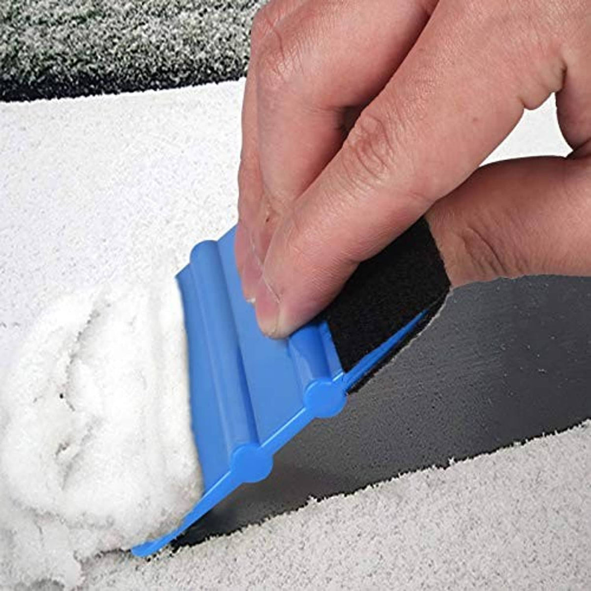 Blue felt edge squeegee with black felt pad, hand trimming along carpet edge