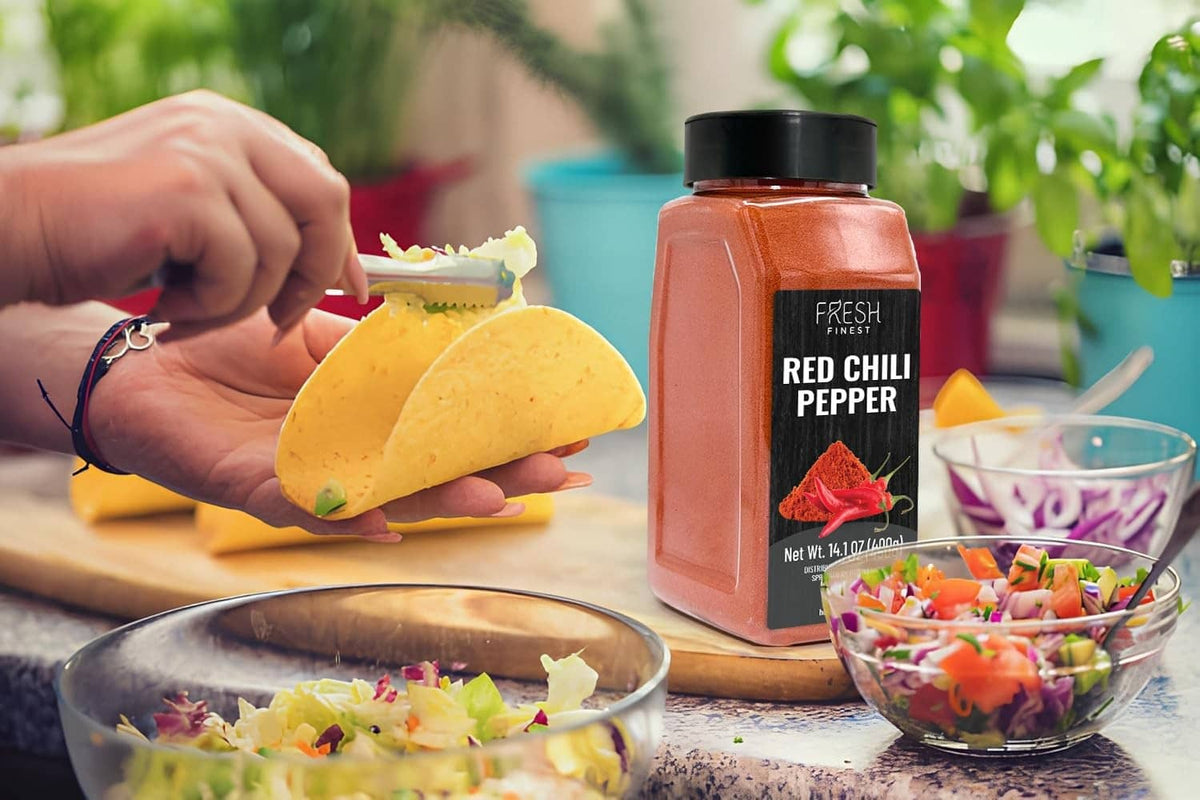 Red chili pepper seasoning jar beside tortilla chips and salad bowl
