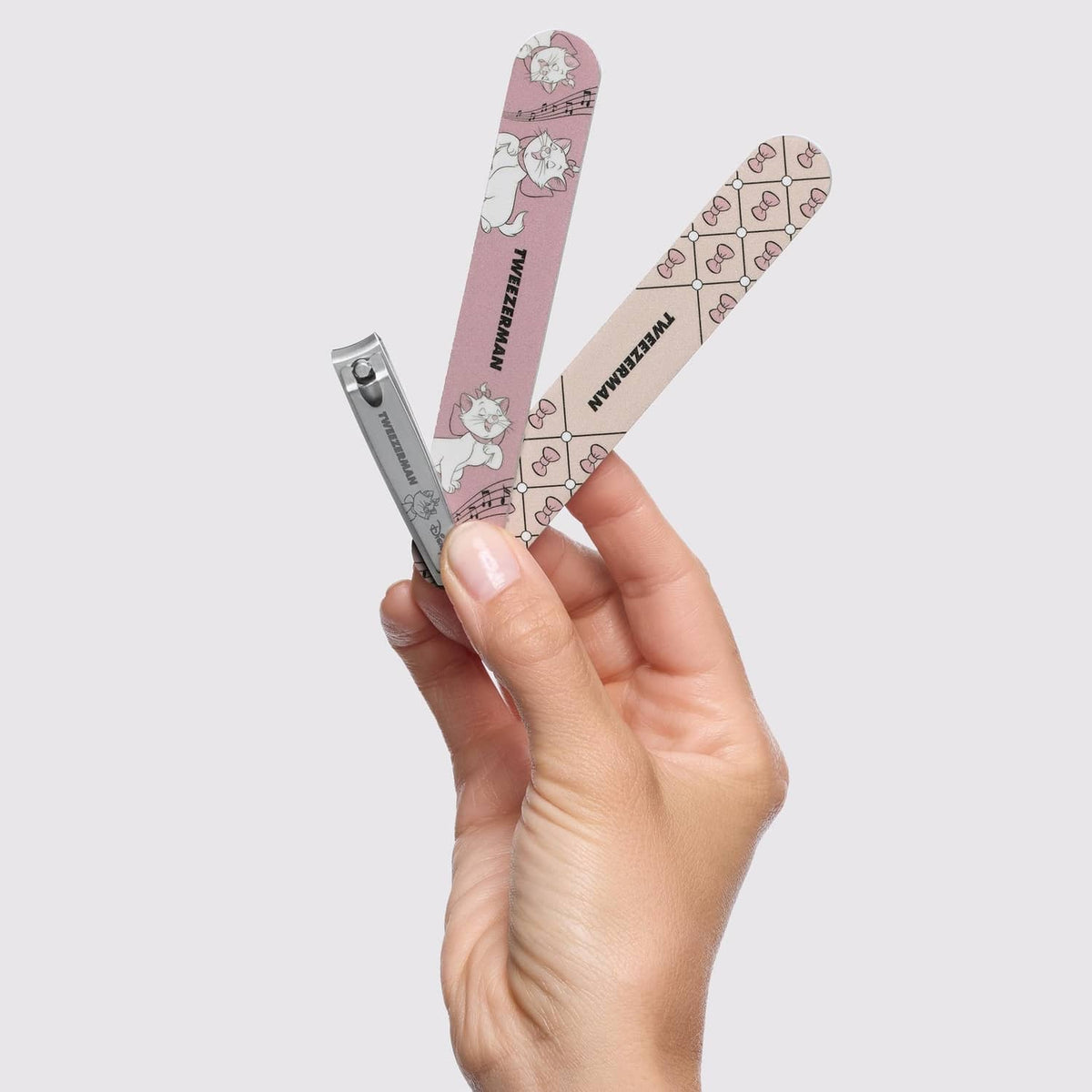 Two pink patterned nail tools with Tweezerman nail clipper in hand