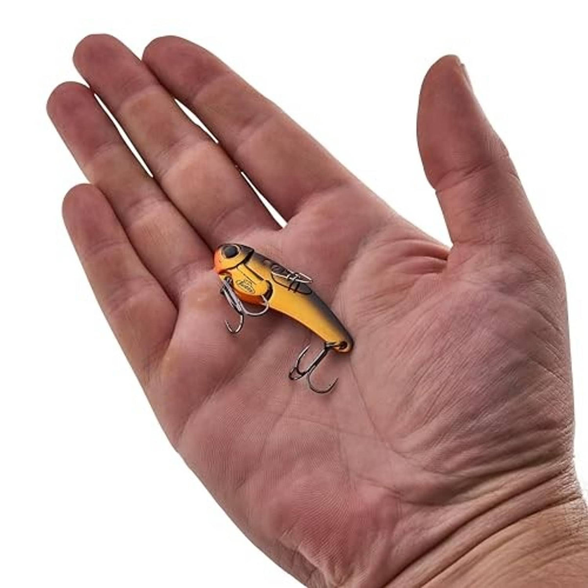 Blade bait fishing lure in hand, yellow-gold metallic body with two treble hooks