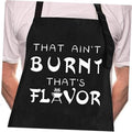 Black chef apron worn over a white shirt with large “That Ain’t Burnt That’s Flavor” print.