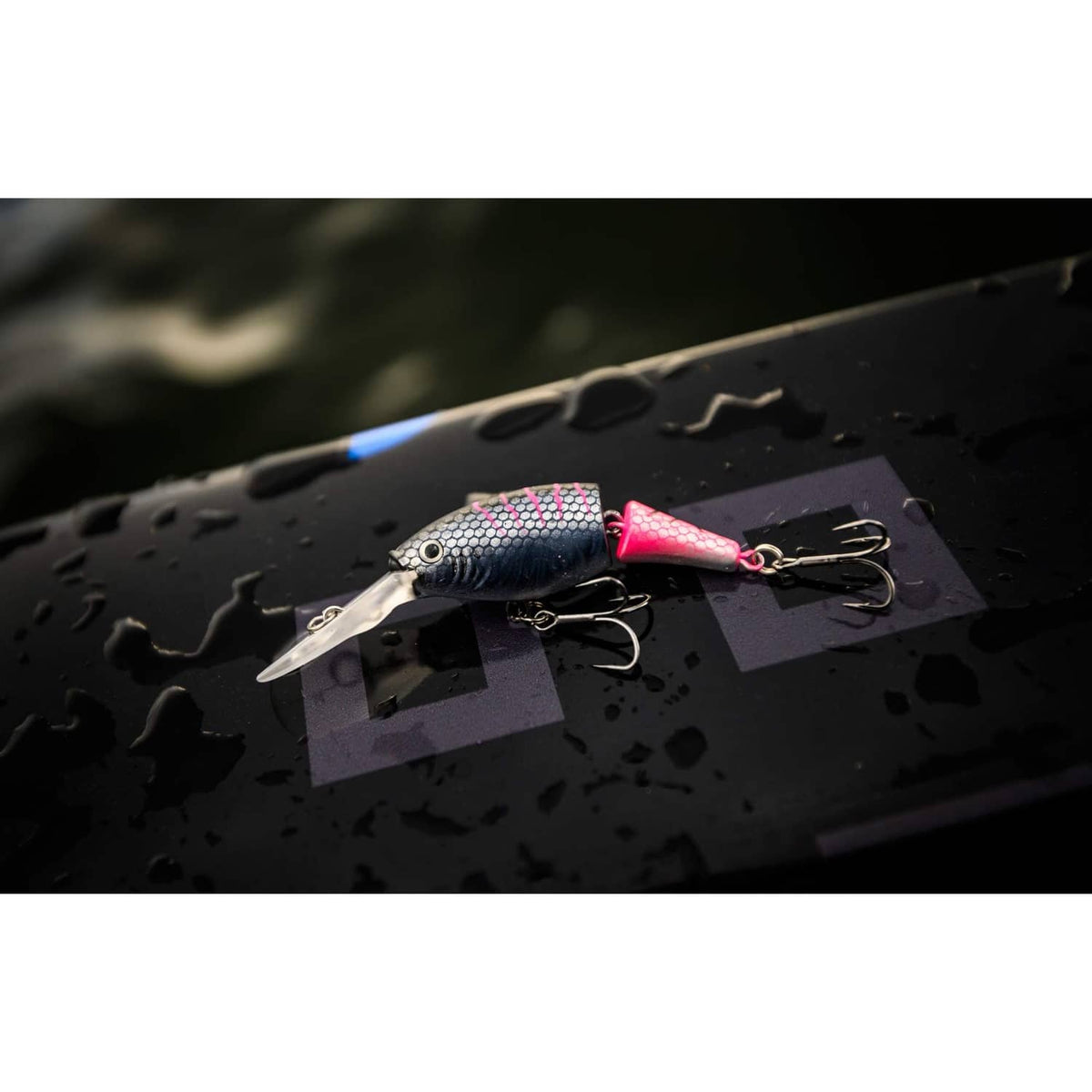 Blue-gray crankbait lure with pink tail and treble hooks on a dark tackle board