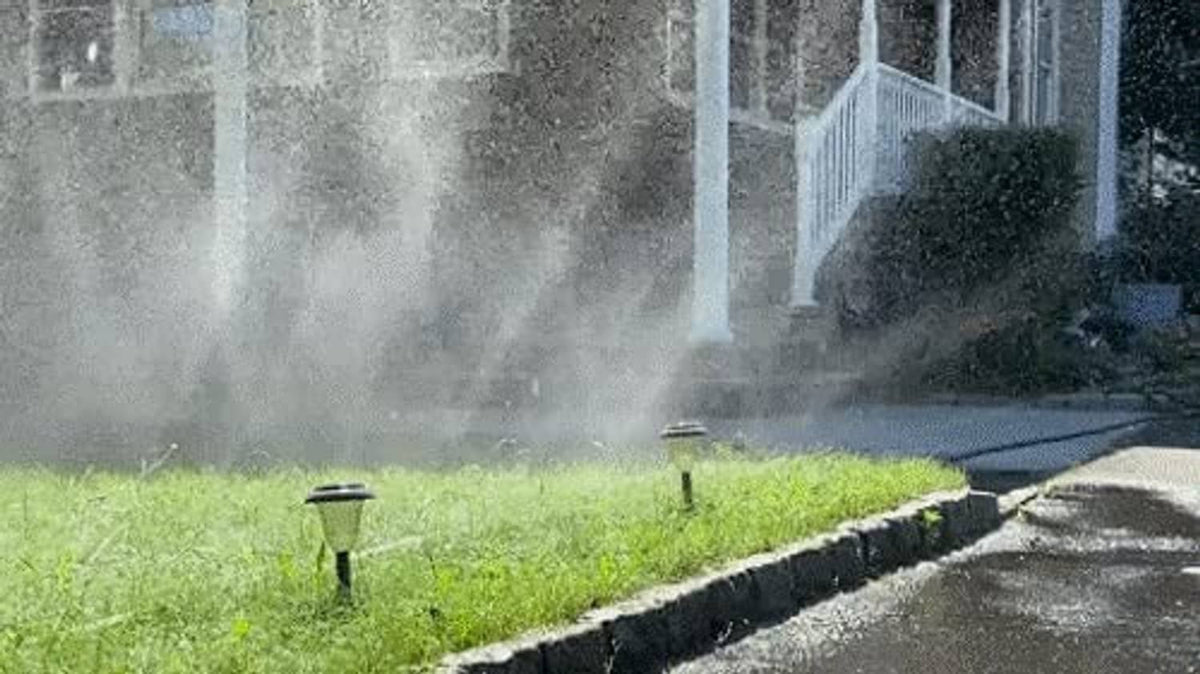 Sprinkler hose heads spraying water in a row along lawn edge
