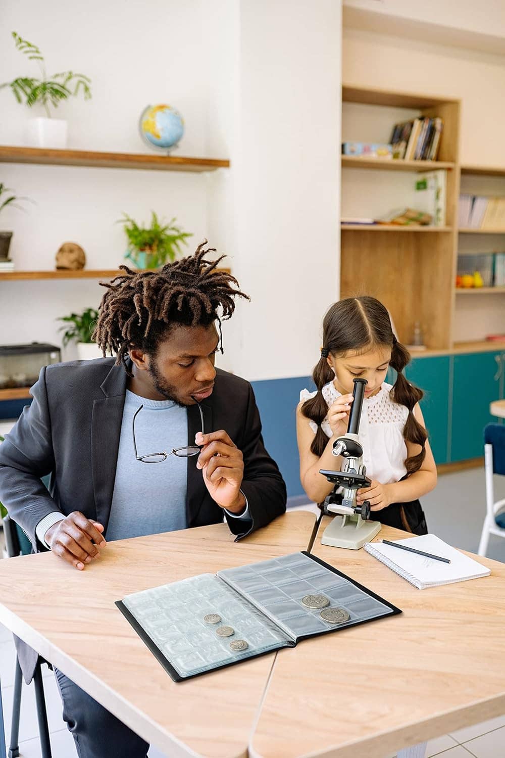 People examining coins using a coin binder and magnifying glass at a table