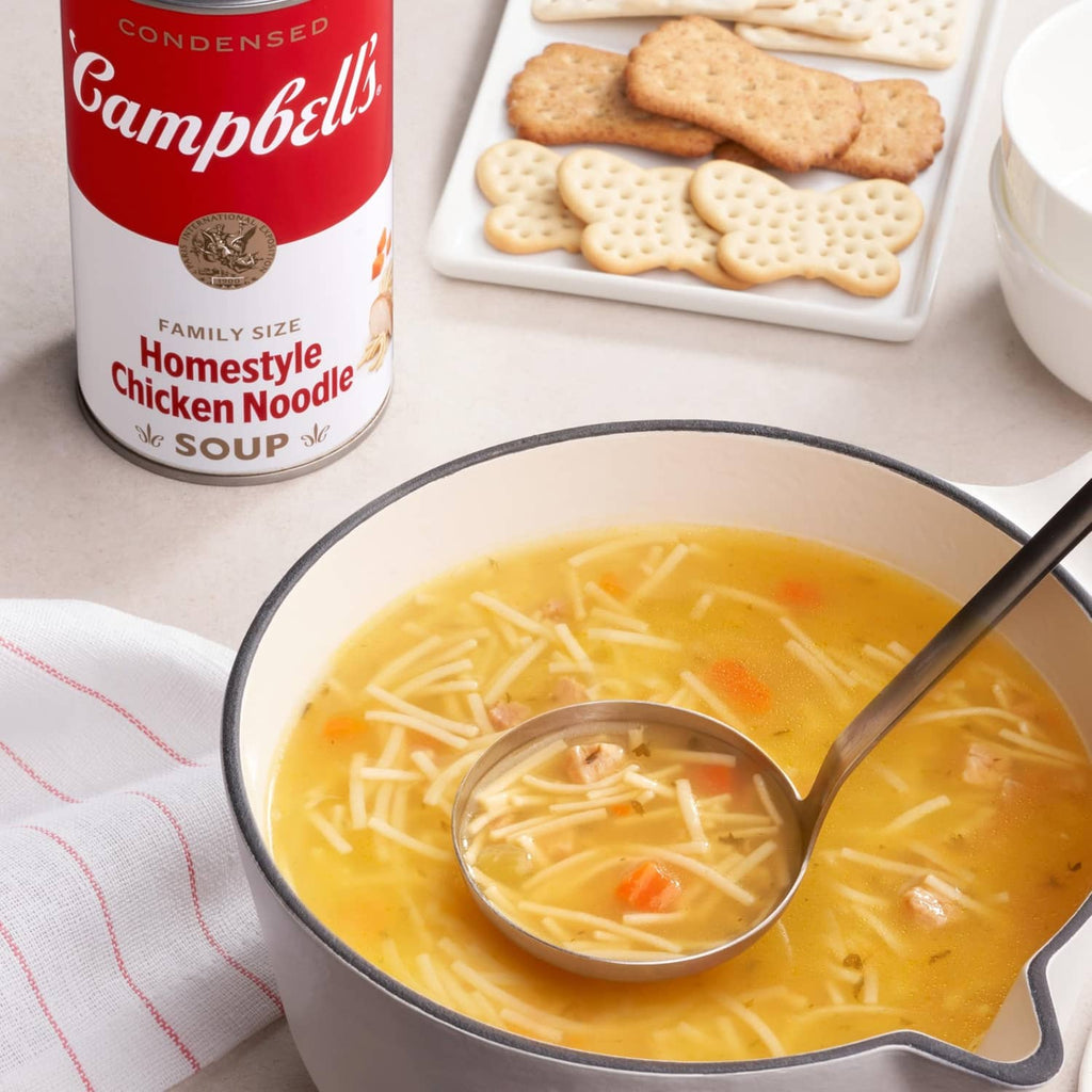 Chicken noodle soup in a pot with crackers and a condensed soup can nearby