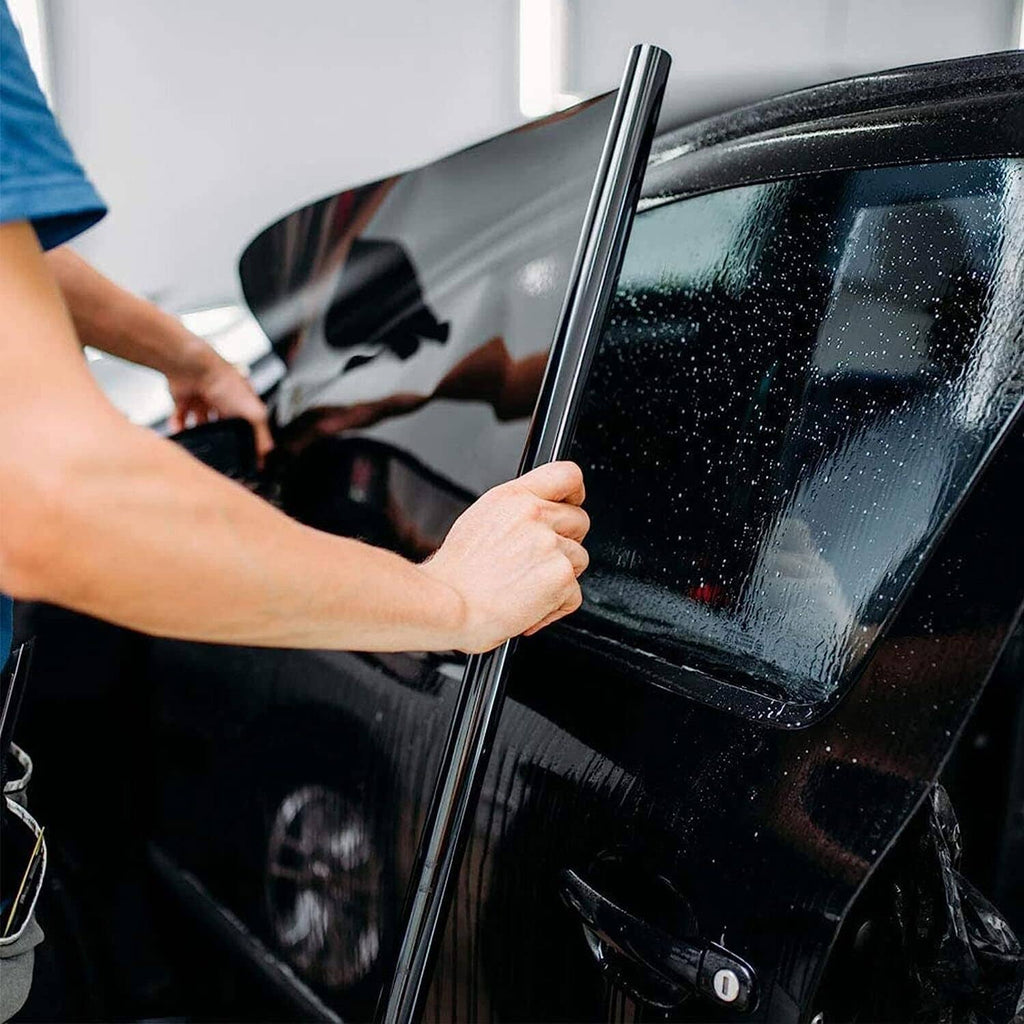 Installer applying dark tint film to car windshield with a squeegee tool