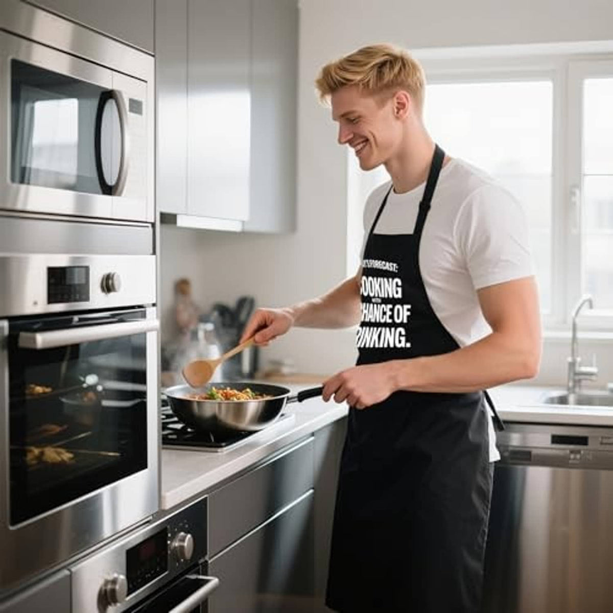 Men's black grill apron with “Cooking” slogan worn while cooking near an oven