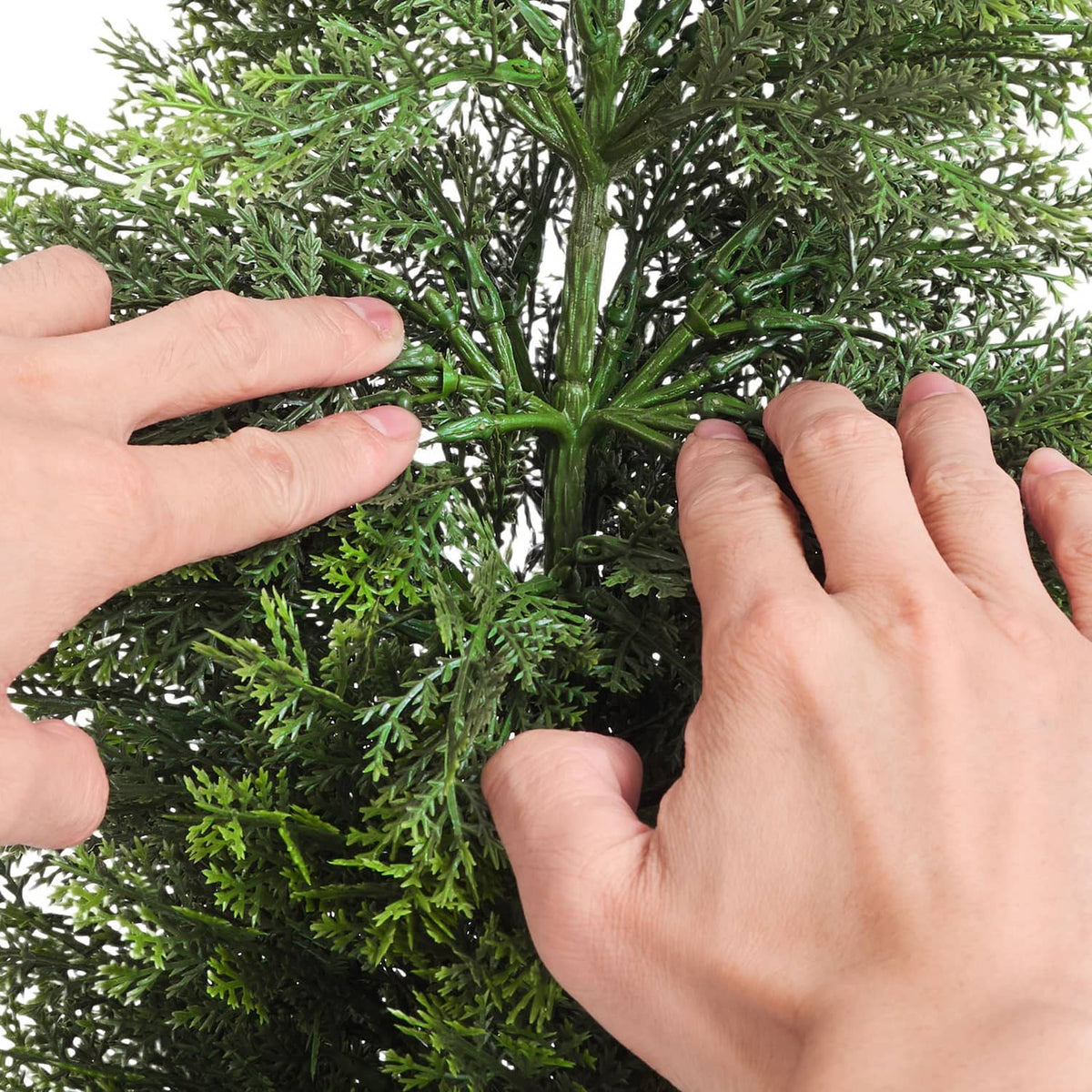 Artificial cedar tree with dense green needles, hands adjusting branches