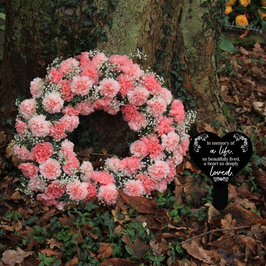 Heart-shaped black remembrance plaque with white verse next to a pink flower wreath.