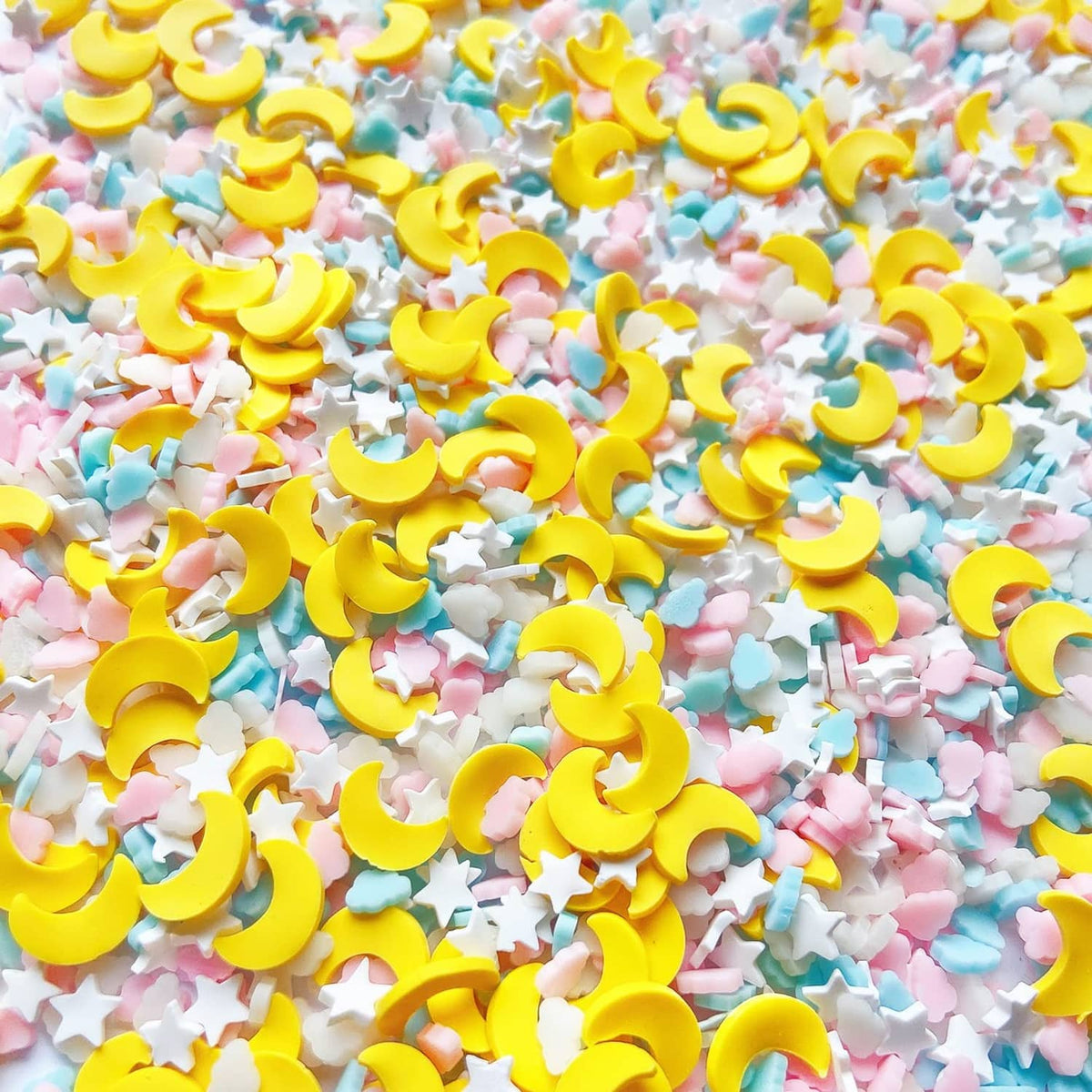 Close-up of small resin confetti sprinkles: yellow crescent moons, pastel clouds