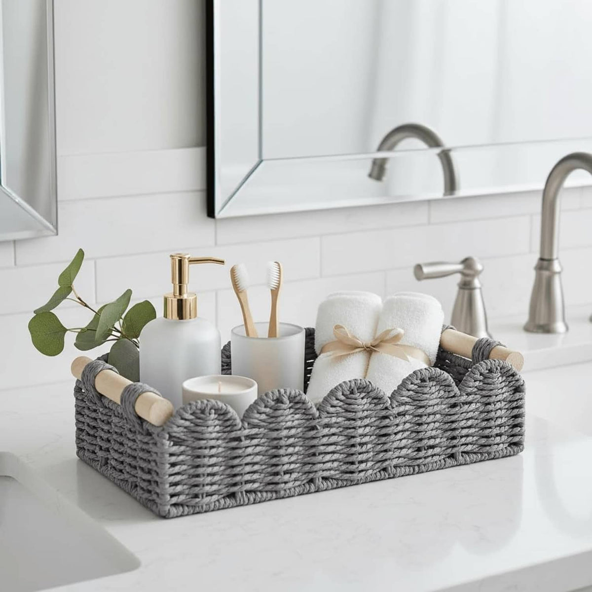 Grey woven toilet paper storage basket with scalloped open top and rope handle ends on sink.