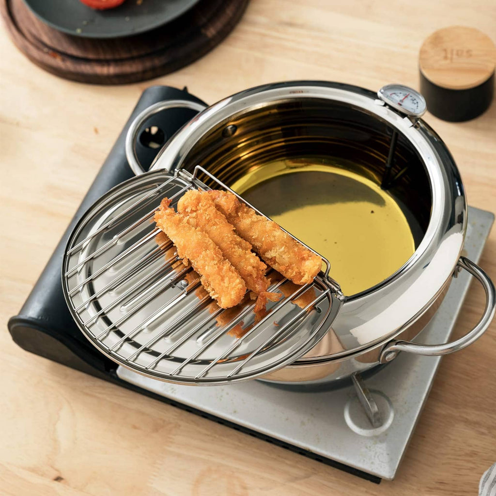 Close-up of stainless steel deep-fryer pot with wire basket and fried chicken above oil