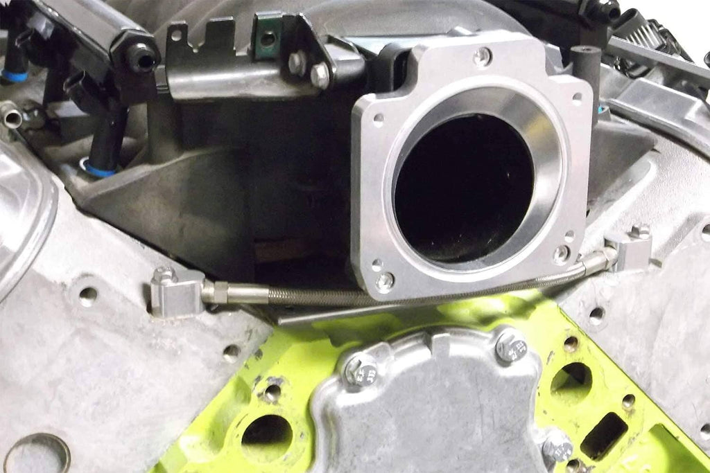 Silver intake spacer or throttle body mount bracket in engine bay with circular opening