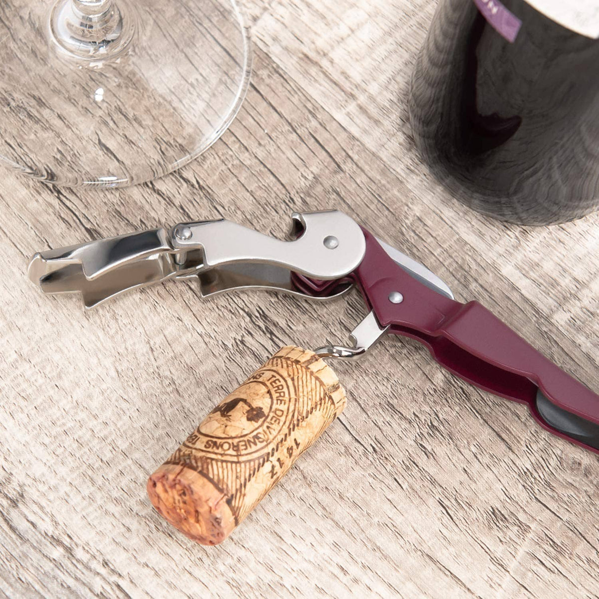 Burgundy wine corkscrew pulling a cork from a wine bottle on a wooden surface