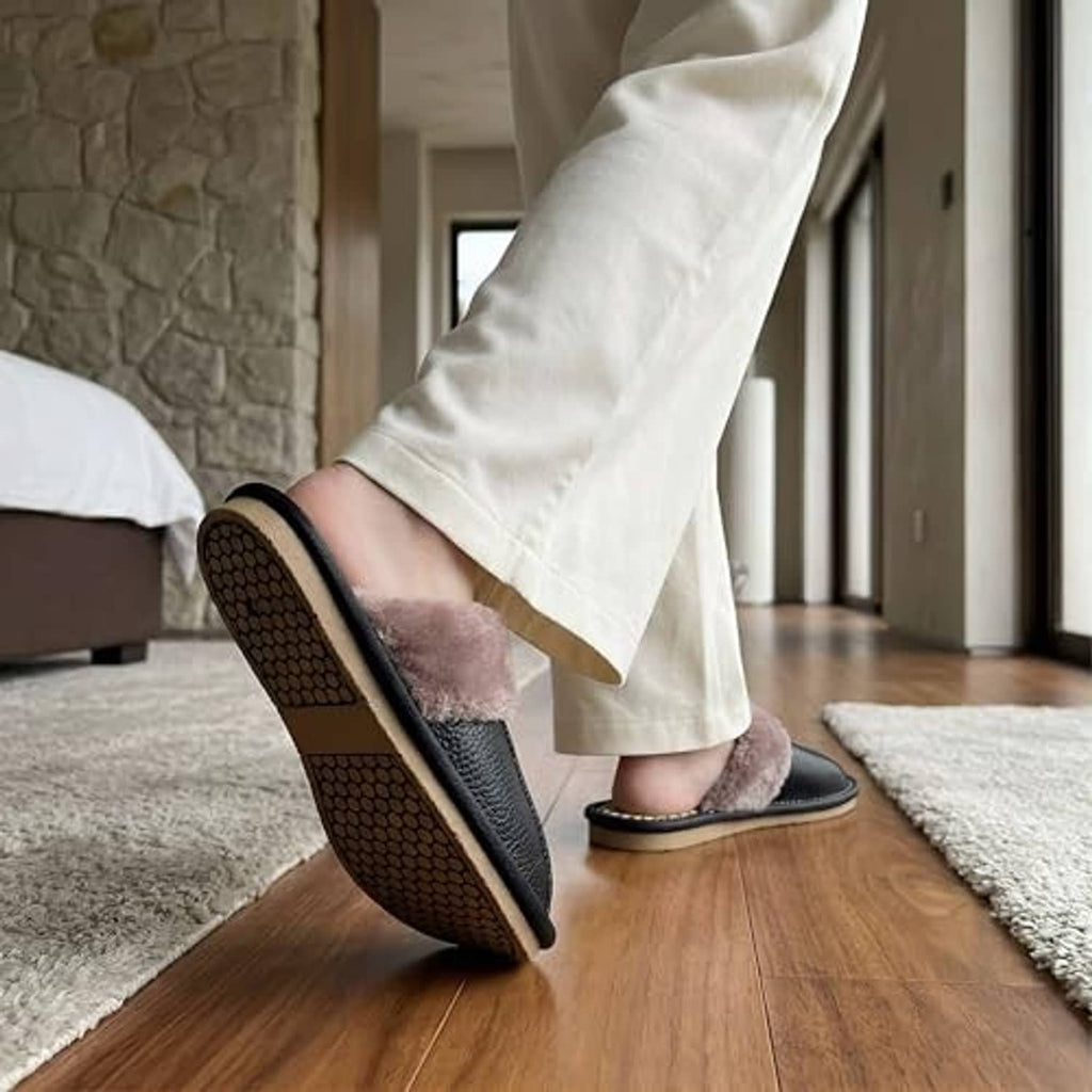 Unisex black leather slippers with plush taupe lining, textured sole, worn indoors.