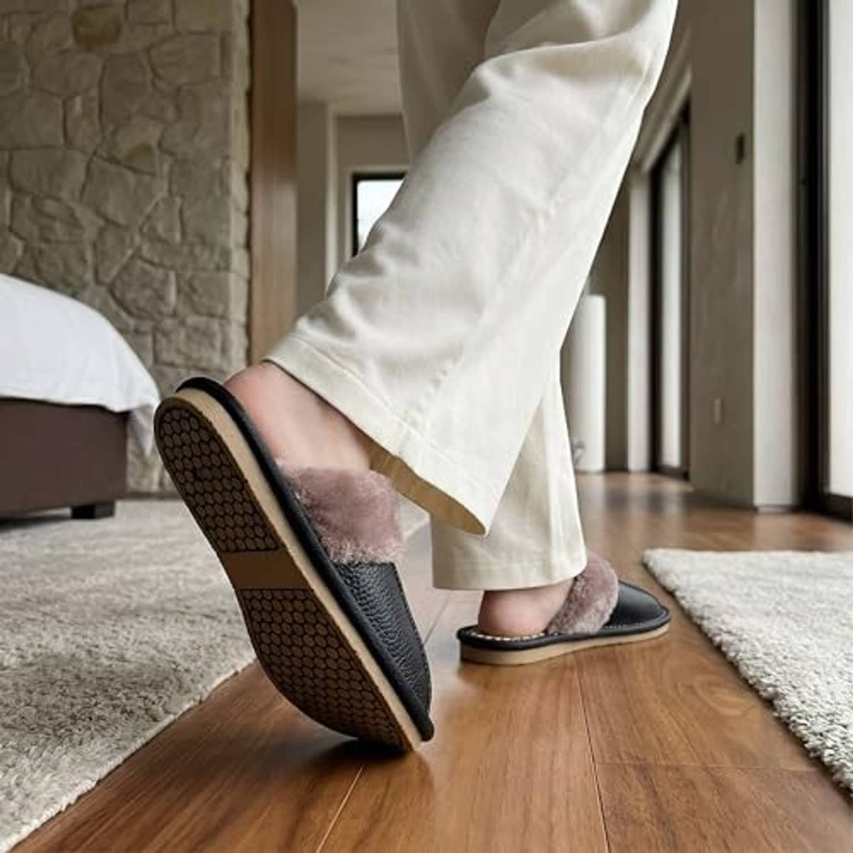 Unisex black leather slippers with plush taupe lining, textured sole, worn indoors.