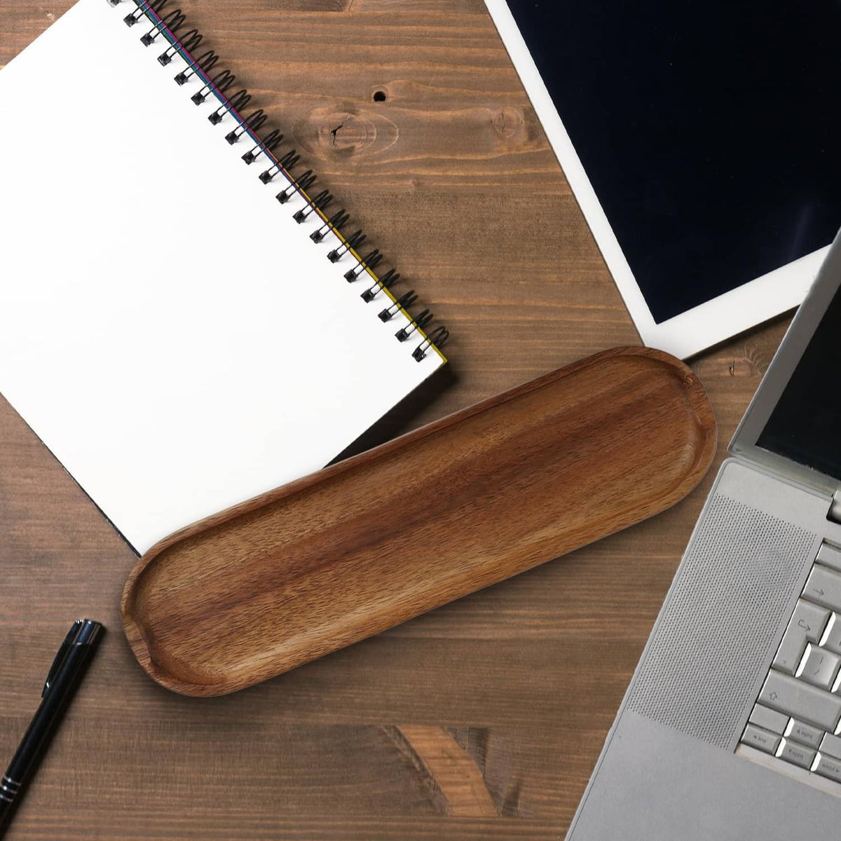 Brown wooden pen tray with pen, placed beside notebooks and keyboard