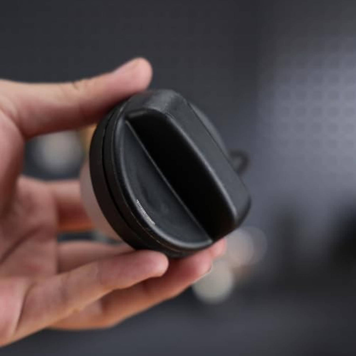 Fuel tank filler cap held in hand, black hinged cover with diagonal ribbing.