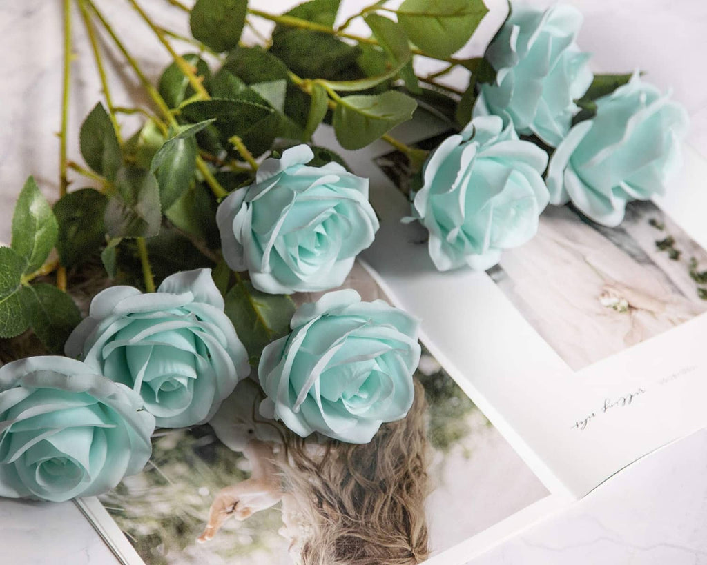Teal blue artificial rose flowers with green leaves arranged with rose stems