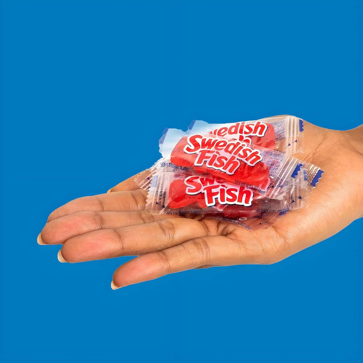 Hand holding an individually wrapped Swedish Fish red gummy candy packet