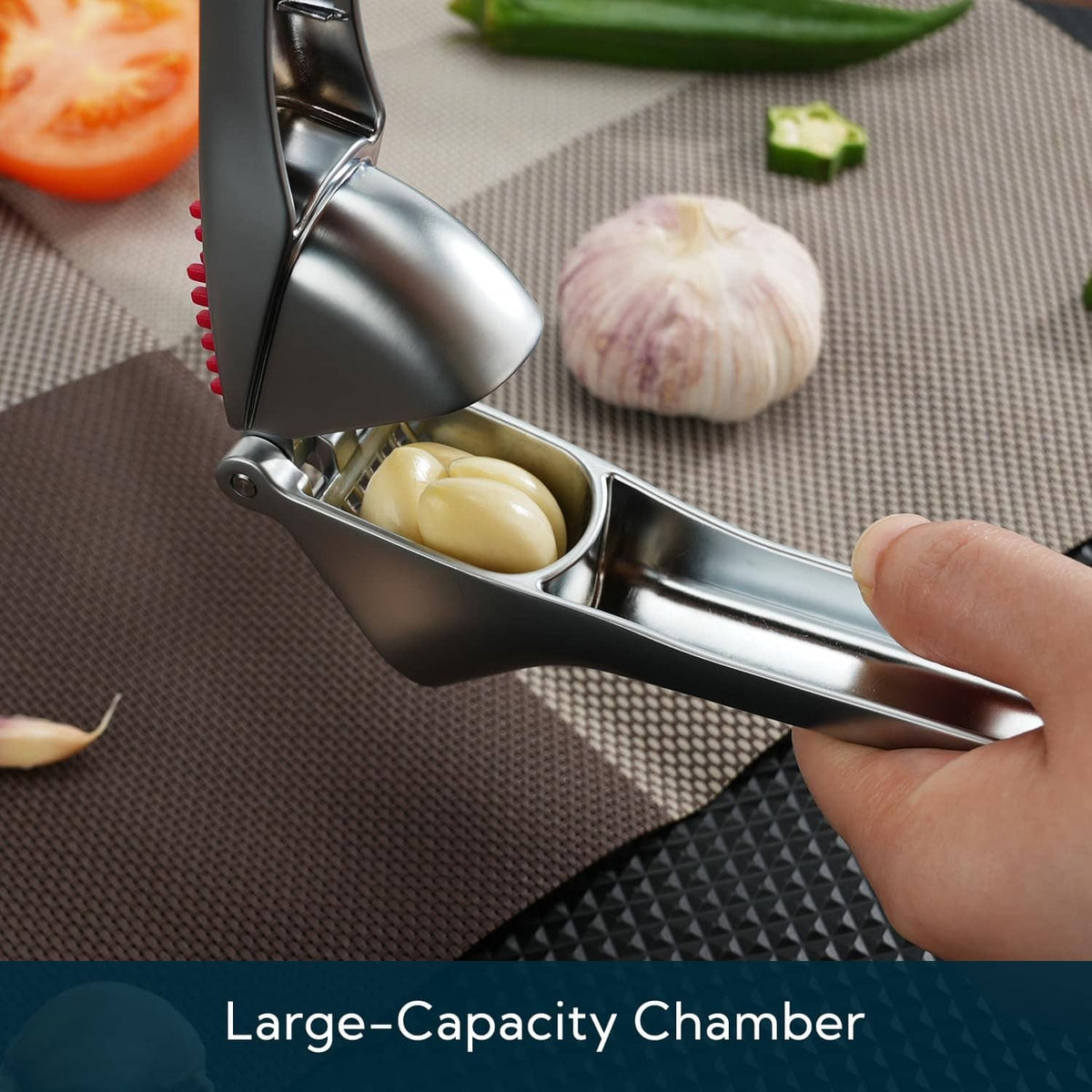 Stainless garlic press with open chamber holding garlic cloves and red scraper