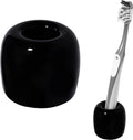 Black ceramic toothbrush holder with toothbrush standing in the round cup; smooth glossy finish.