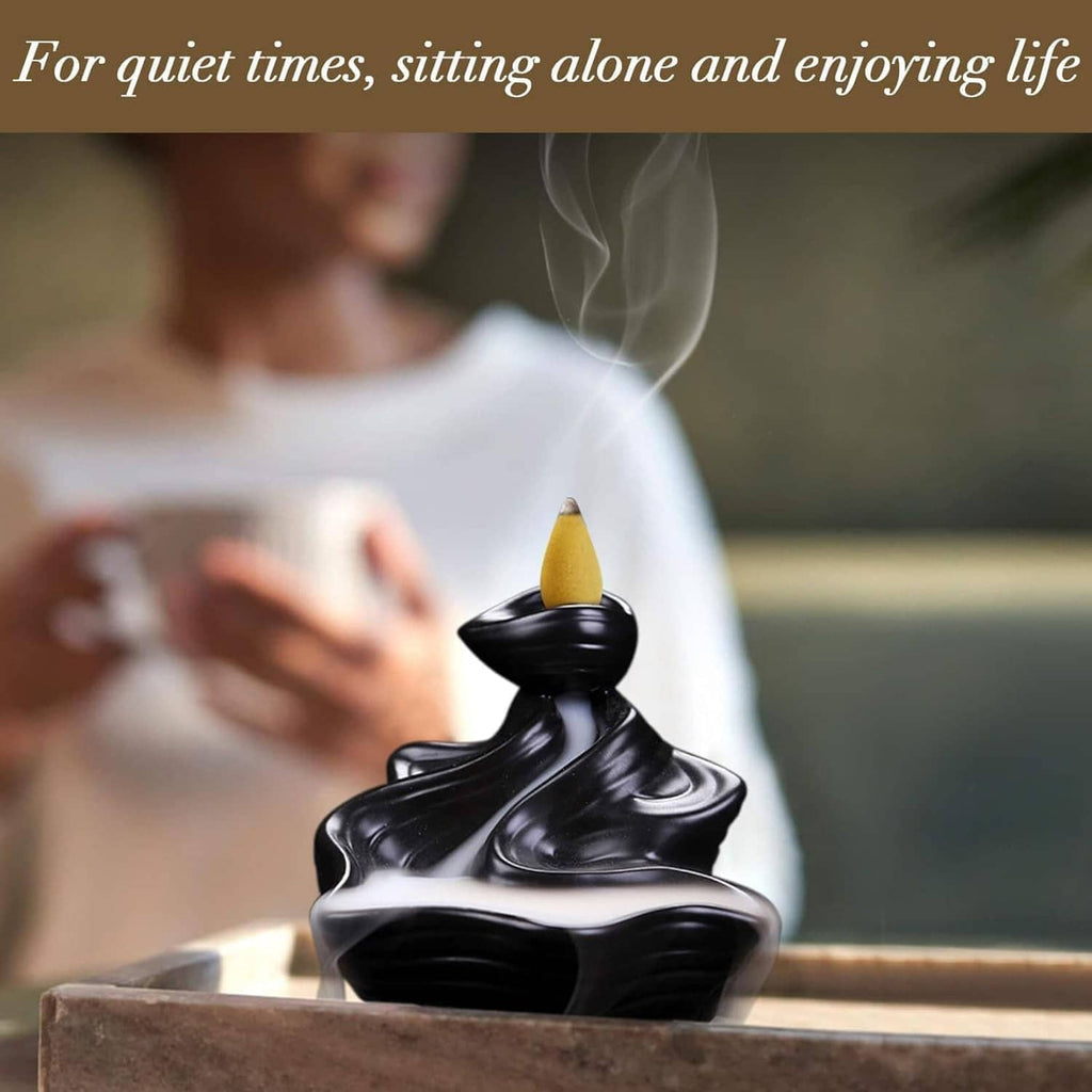 Black backflow incense burner with a yellow cone emitting smoke