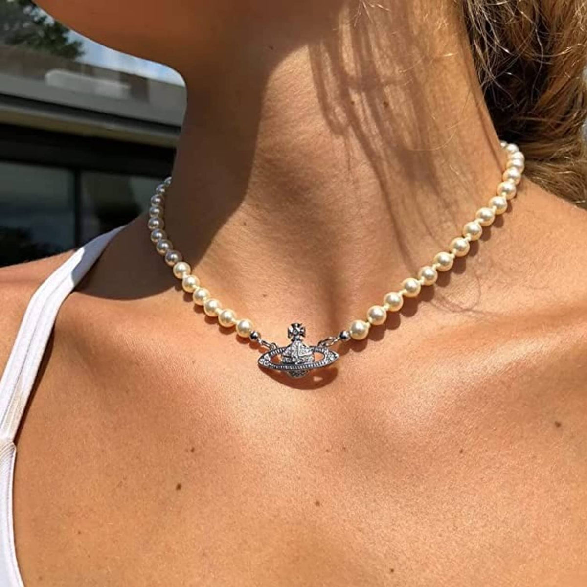 White pearl choker with silver Saturn pendant charm, close-up at collarbone