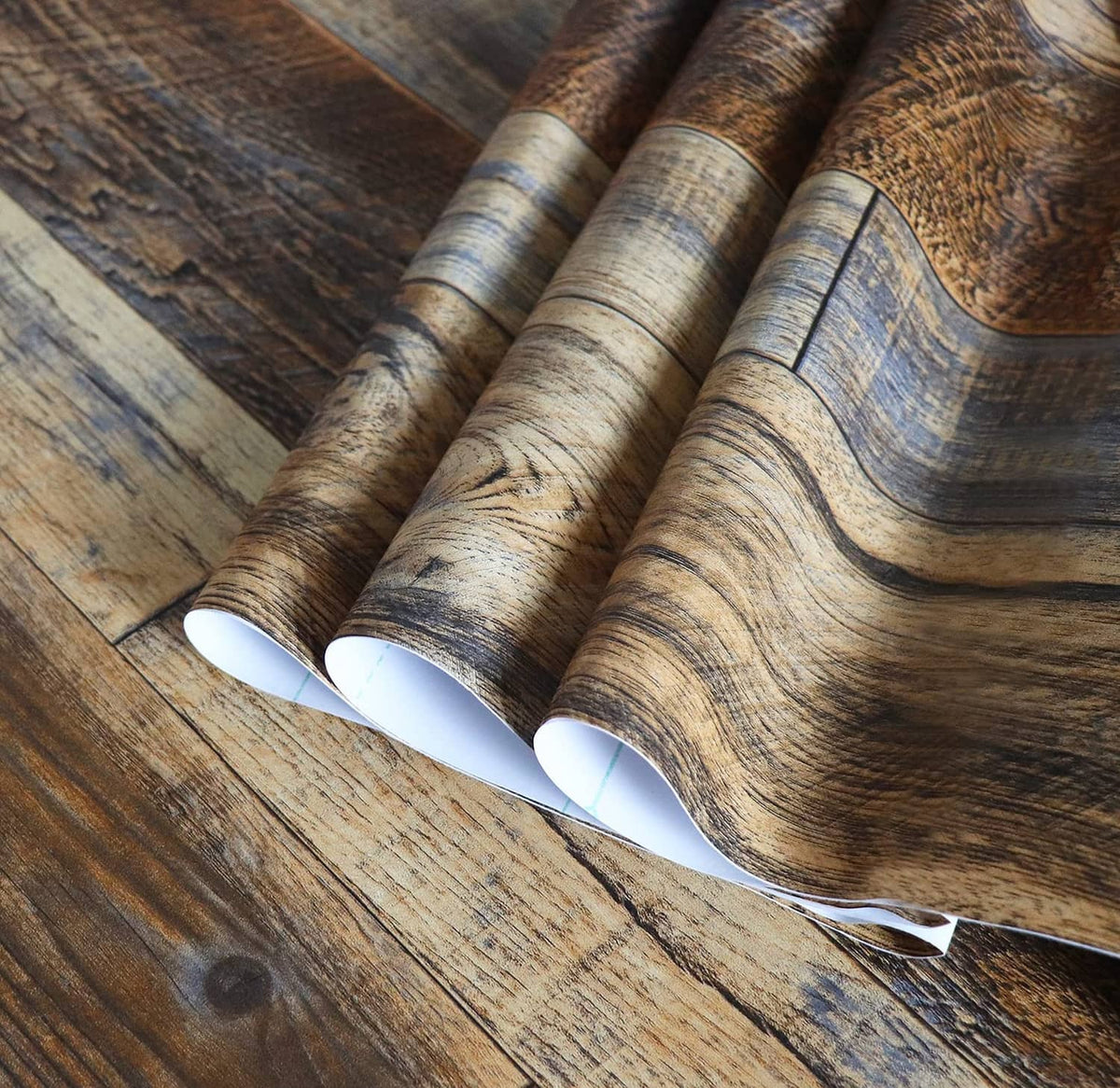 Faux wood peel-and-stick wallpaper roll with brown and blue plank pattern and curled backing