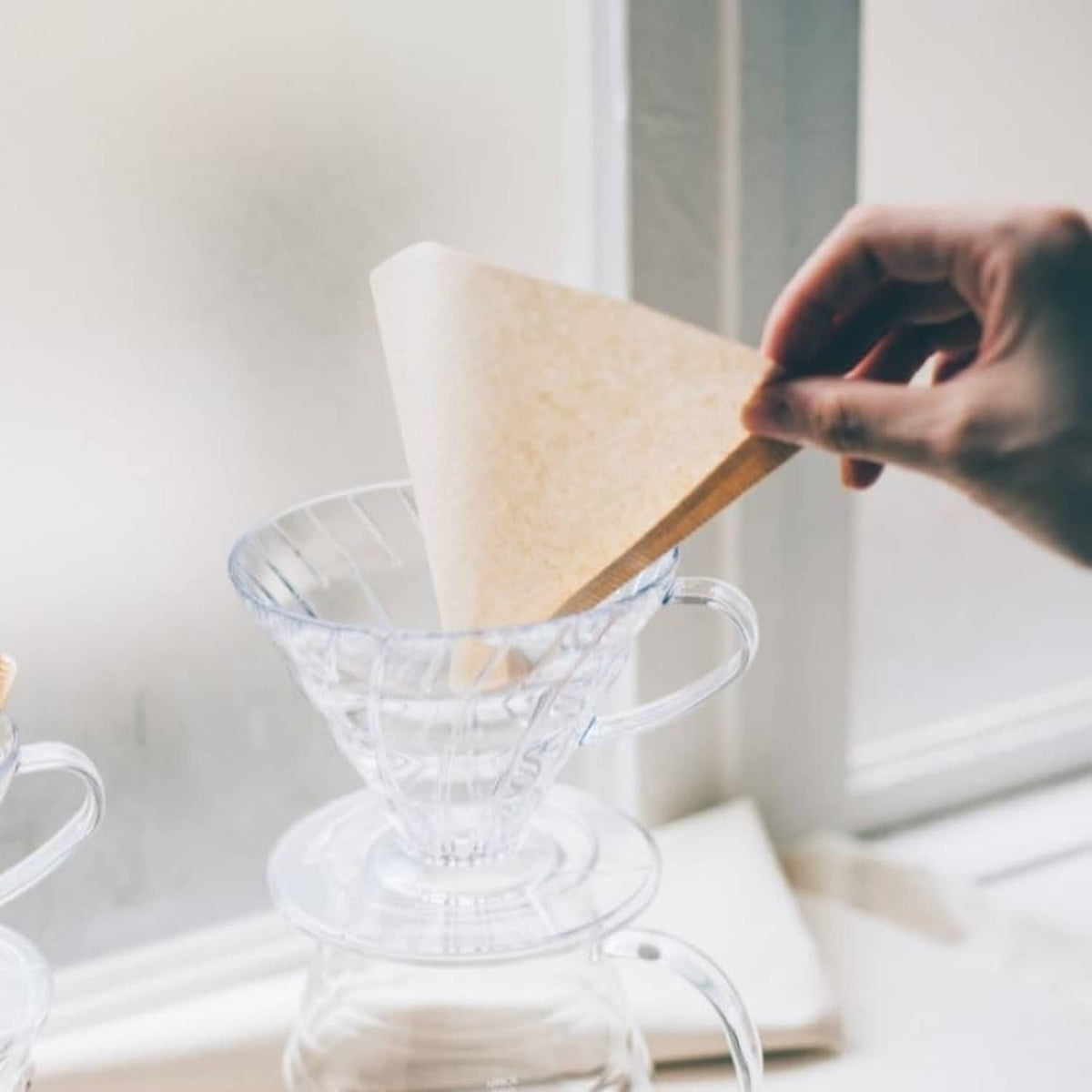 Hand inserting a natural paper coffee filter into a clear dripper