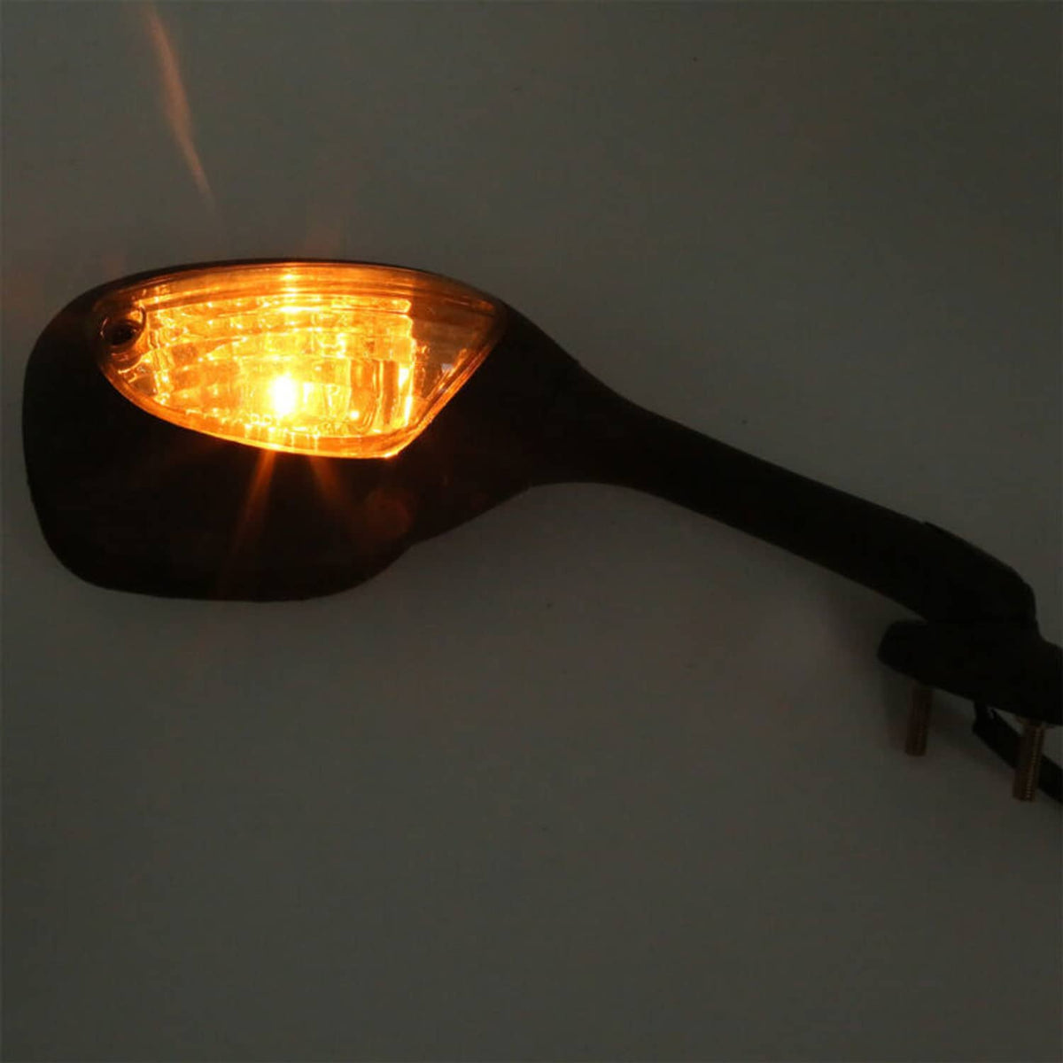 Close-up of black motorcycle mirror showing lit amber turn signal lens