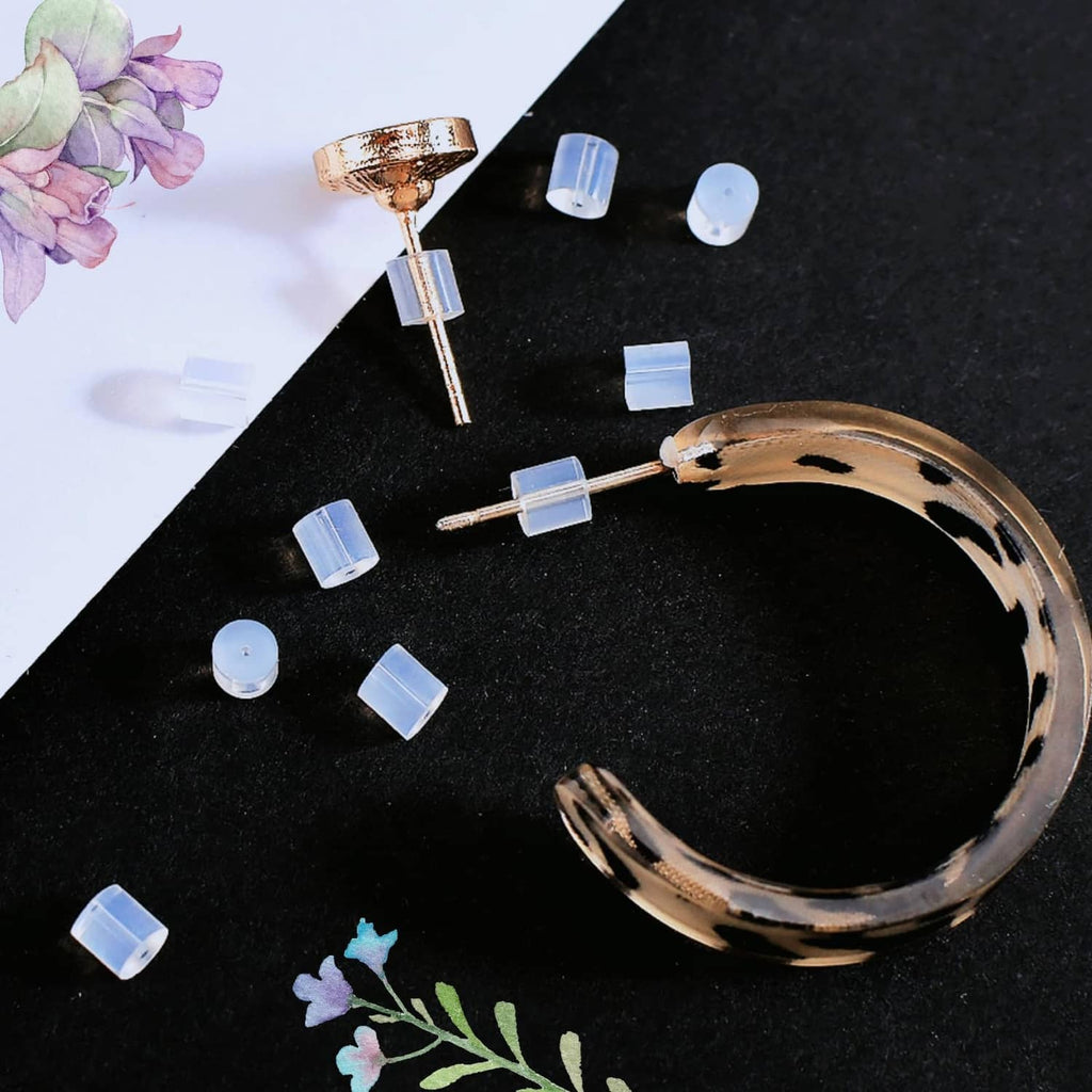 Clear silicone earring backs near stud posts, small transparent cylinder stoppers